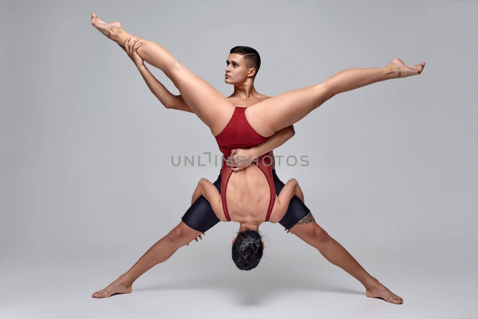 The pair of a modern ballet dancers are posing against a gray studio background. Strong man in black shorts and tiny woman in a red swimwear are dancing together. Ballet and contemporary choreography concept. Art photo.