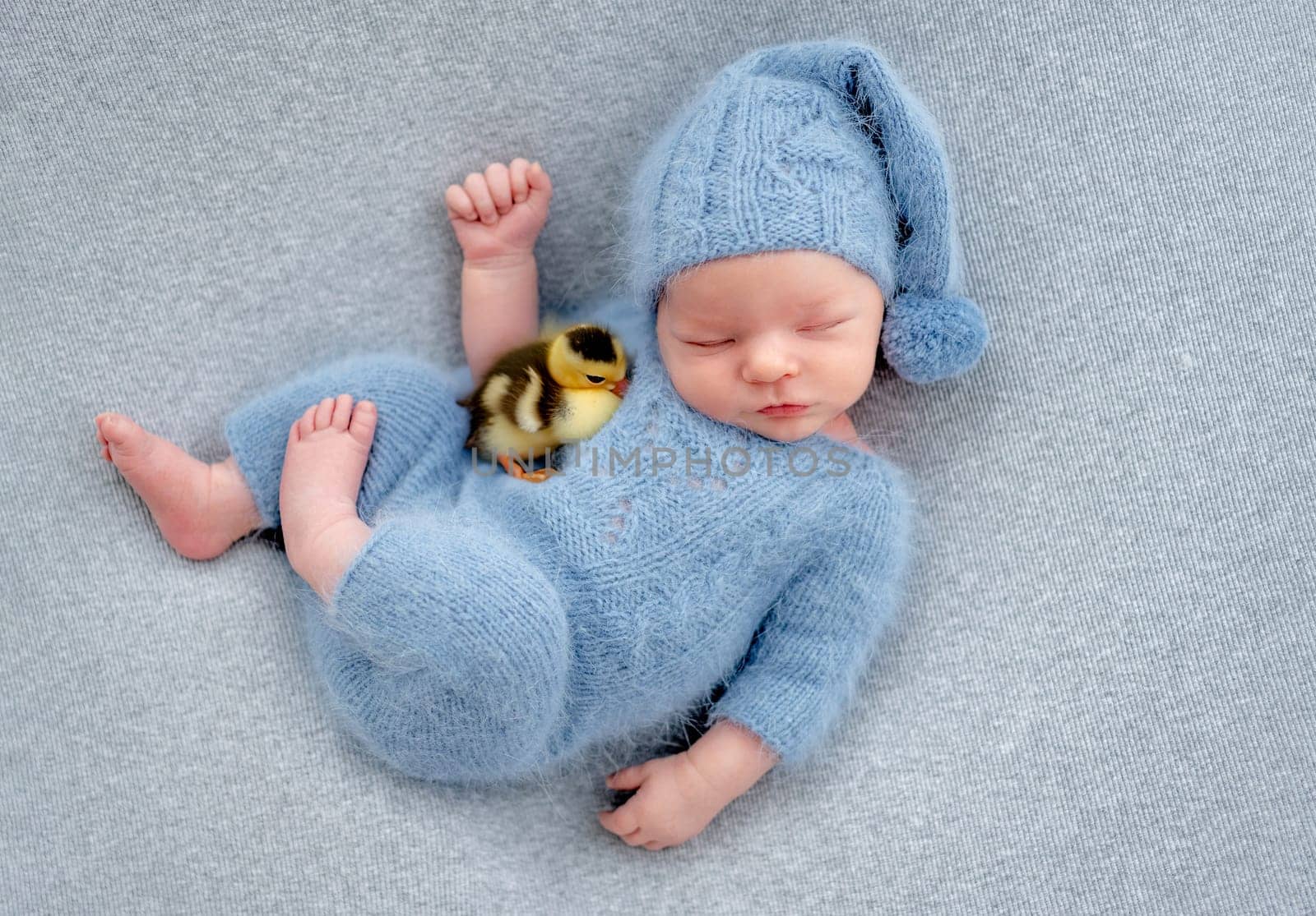 Newborn baby boy sleeping with a duckling chick. Adorable infant child kid sleeping wearing knitted hat and costume