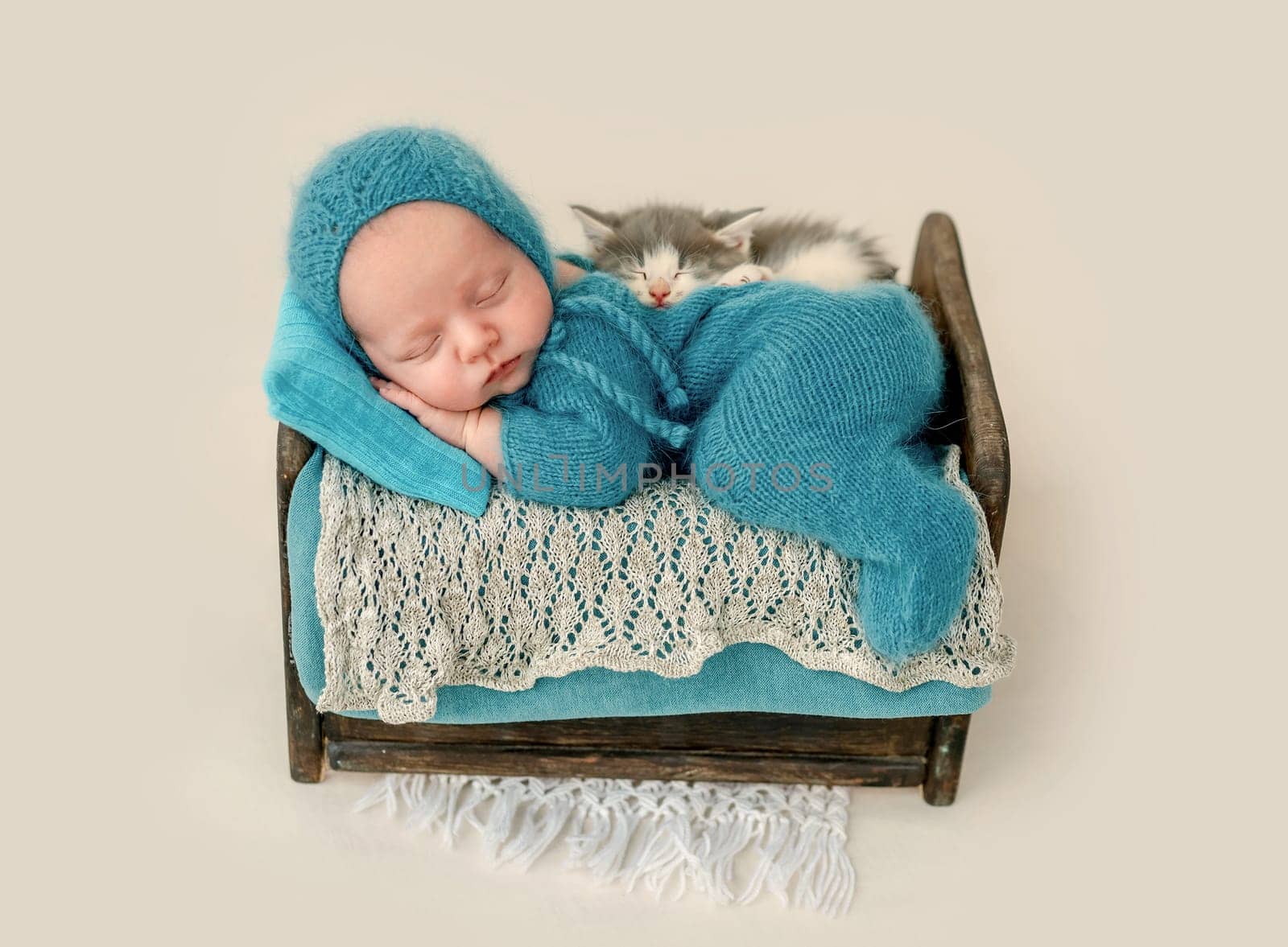 Newborn baby boy with kitty sleeping and holding hands under his cheeks. Infant kid napping in tiny bed