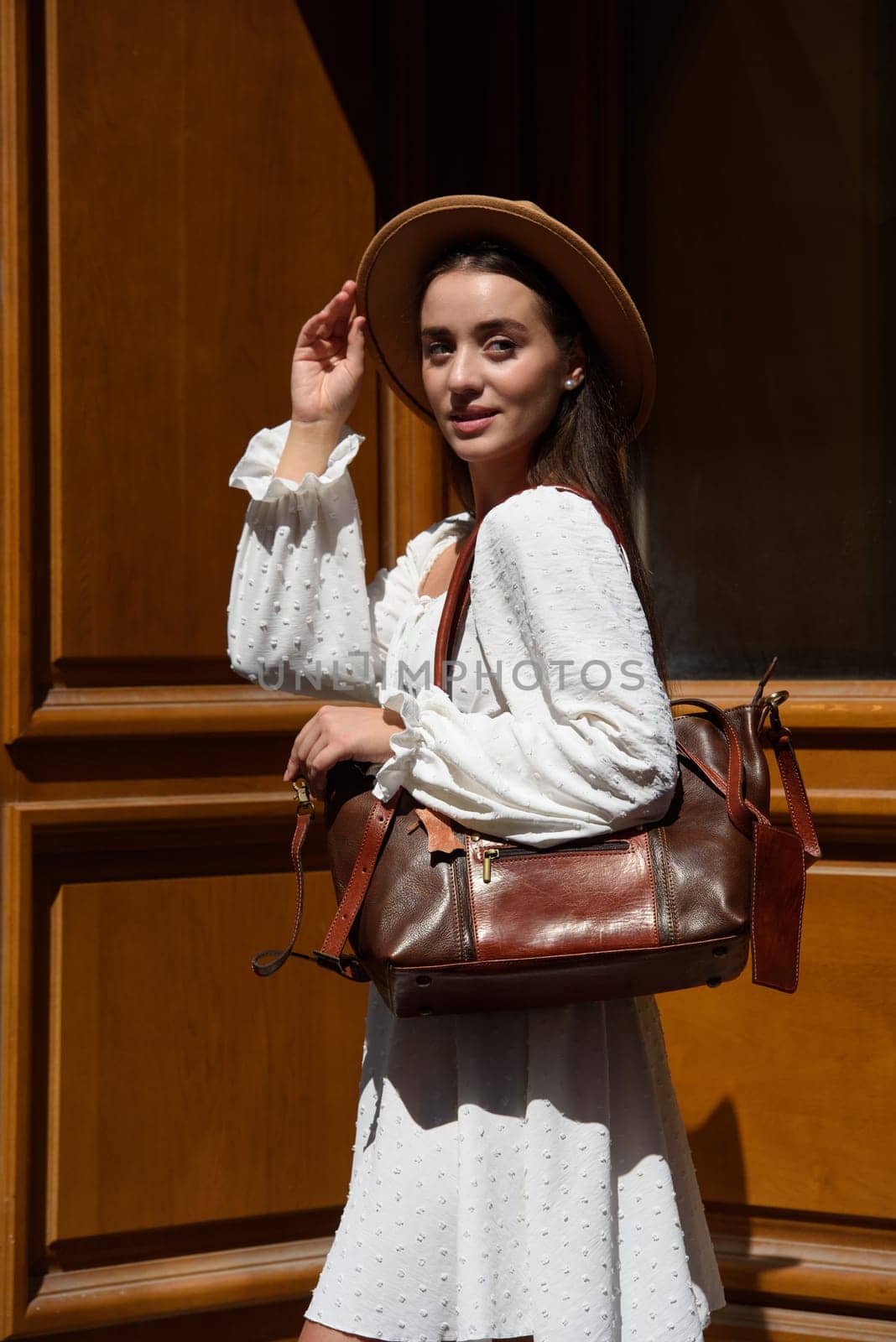 brunette with long hair wearing white romantic summer dress and beige hat posing with luxury leather bag by Ashtray25