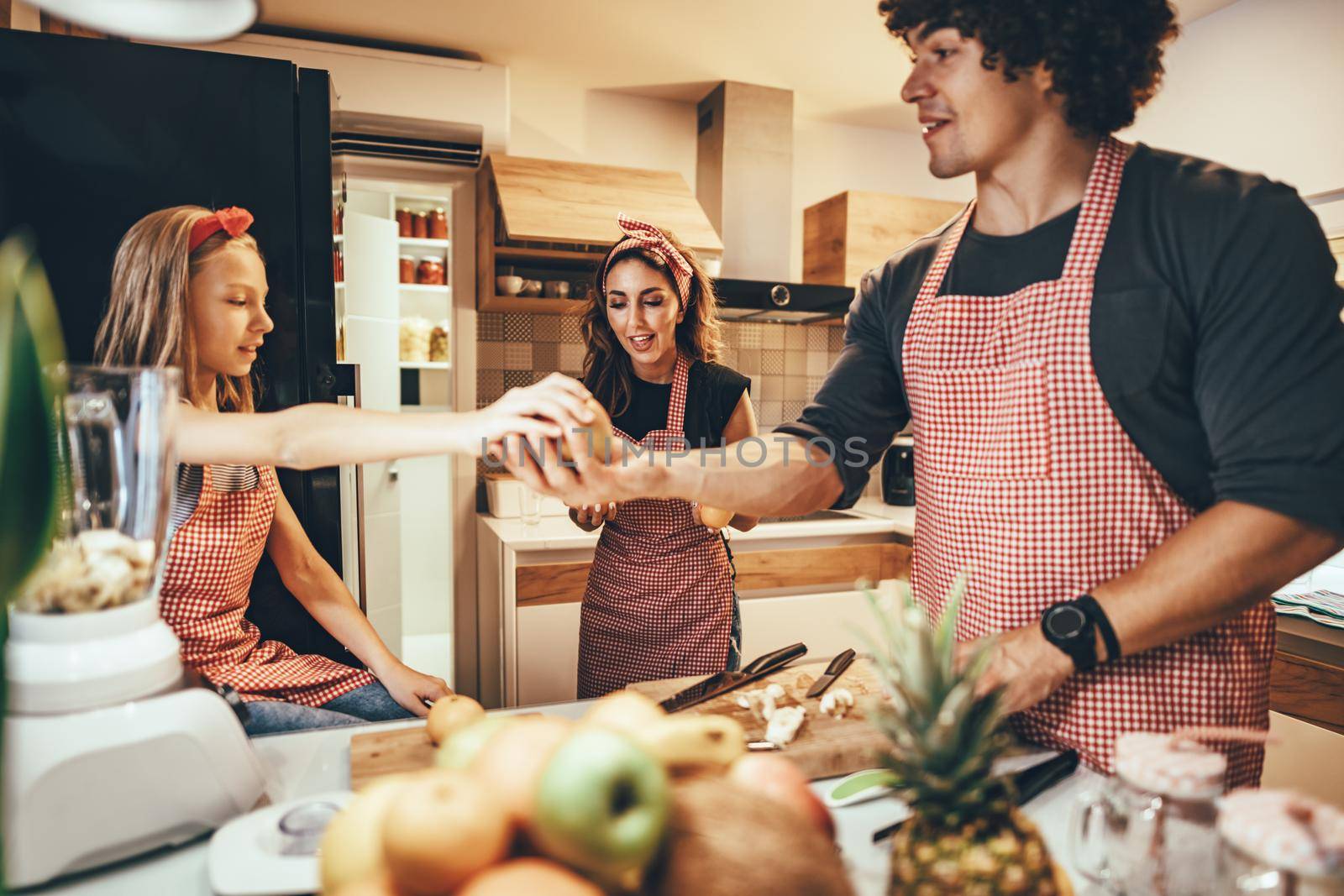 Happy father and his daughter enjoy and having fun in making and having healthy meal together at their home kitchen. Smiling mother is helping them.