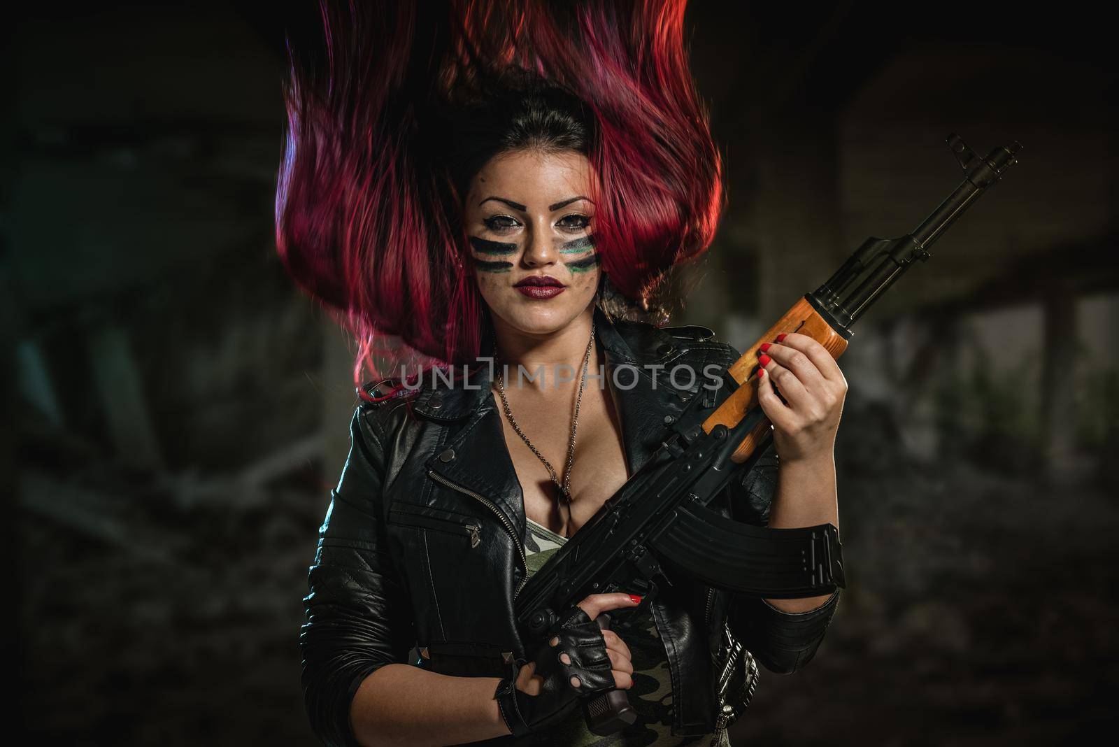 Young attractive military woman with face paint in war paint holding rifle and looking at camera.