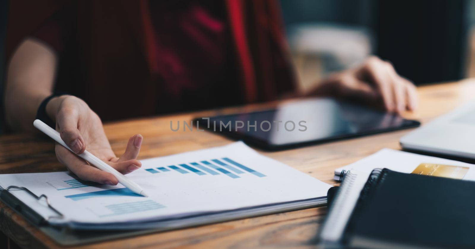 Close up business woman holding pen and pointing paper chart summary analyzing annual business report with using laptop at room office desk.