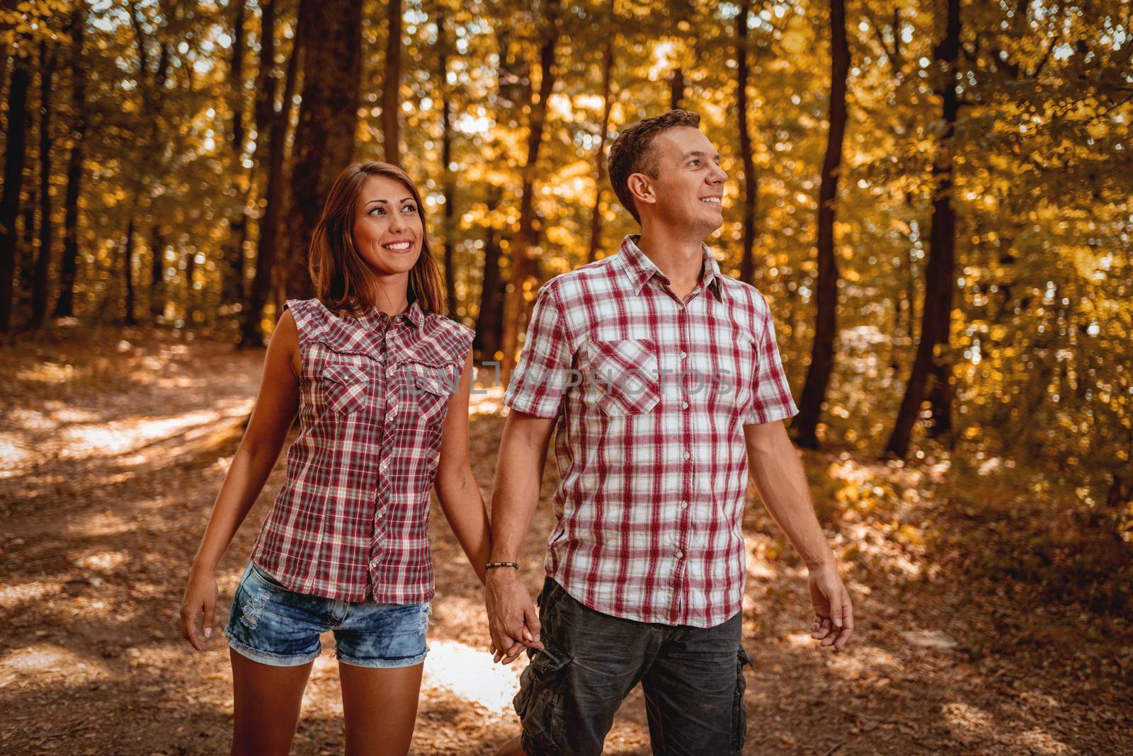 Beautiful young couple are walking in the forest and enjoying in the autumn sunny day. 