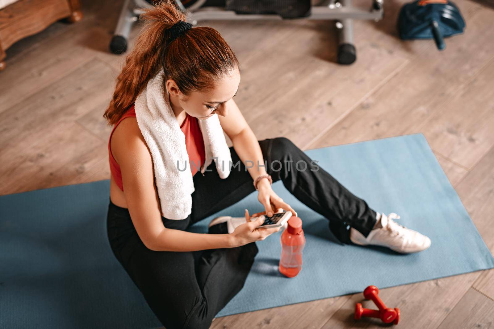 Attractive woman using a smartphone while taking break of exercising in living room at home.