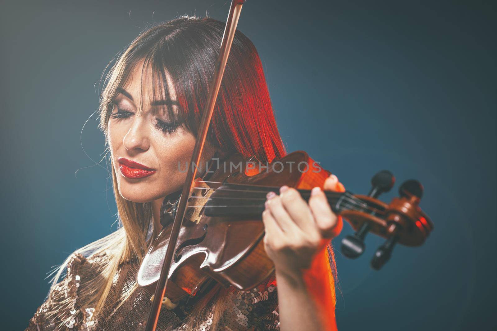 Beautiful young smiling woman in sequin dress playing the classical music on violin.