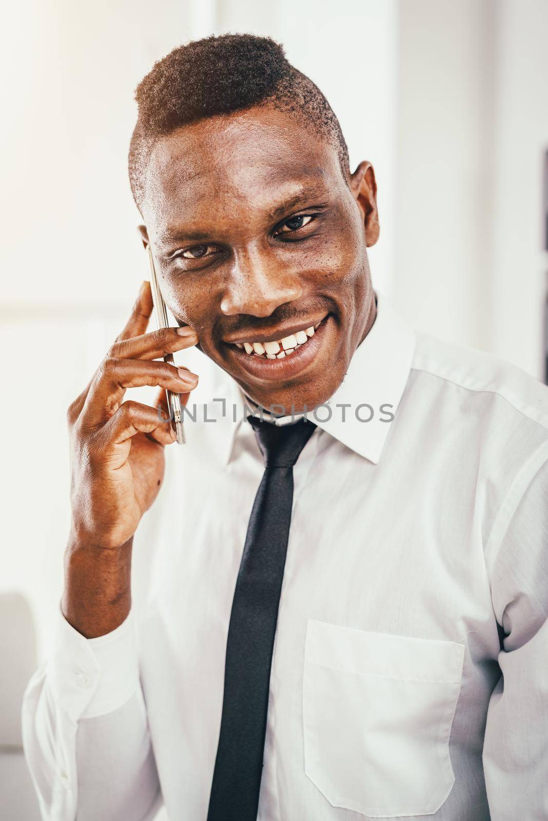 A portrait of a satisfied African businessman who is talking on smartphone in modern office.