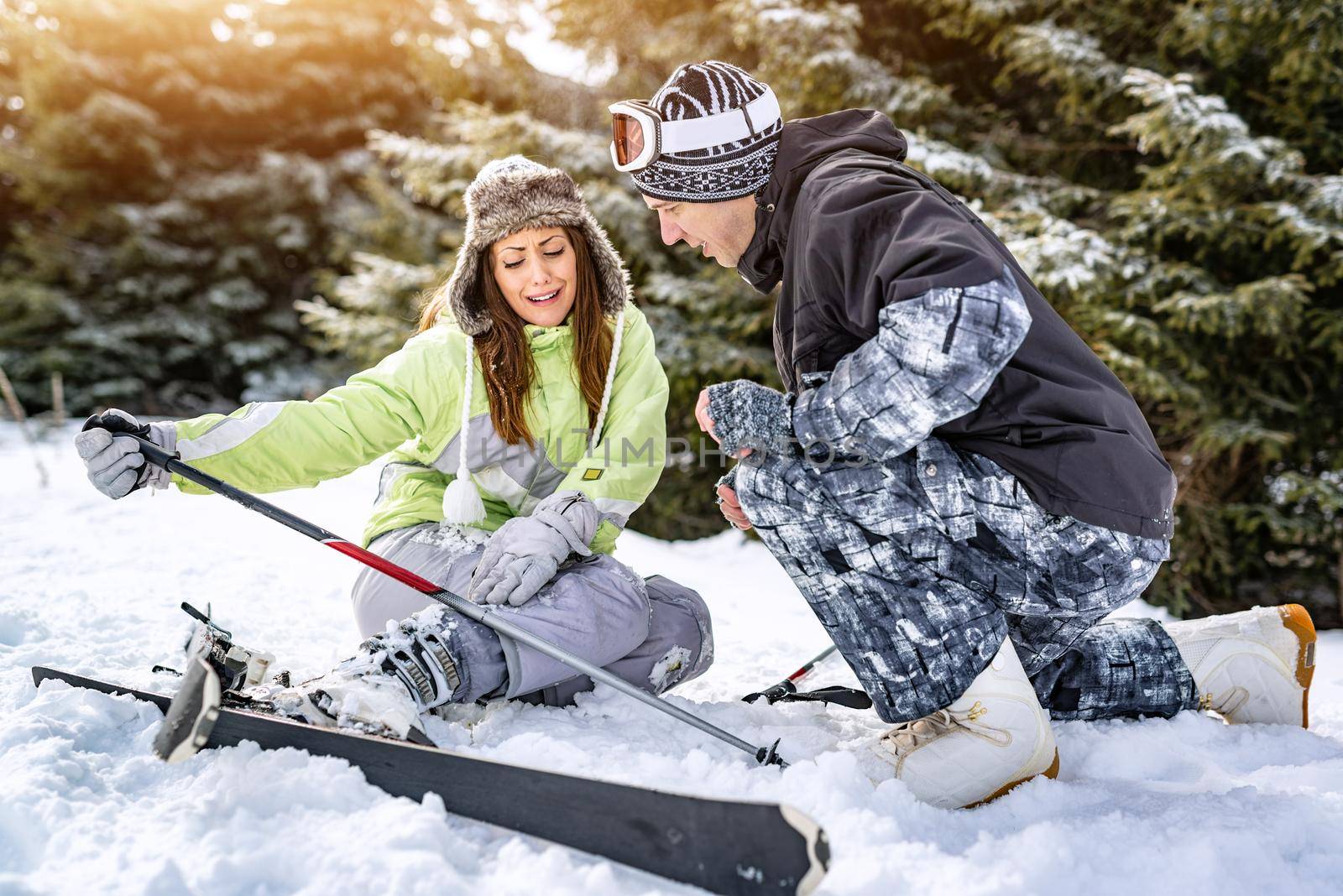 Young man snowboarder helps a beautiful young female skier who fell down on mountain slope.