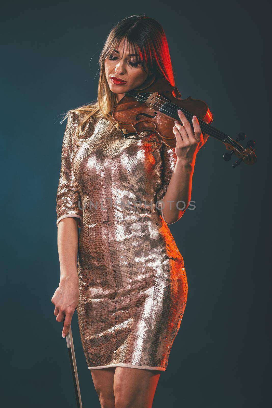 Beautiful young smiling woman in sequin dress playing the classical music on violin.  