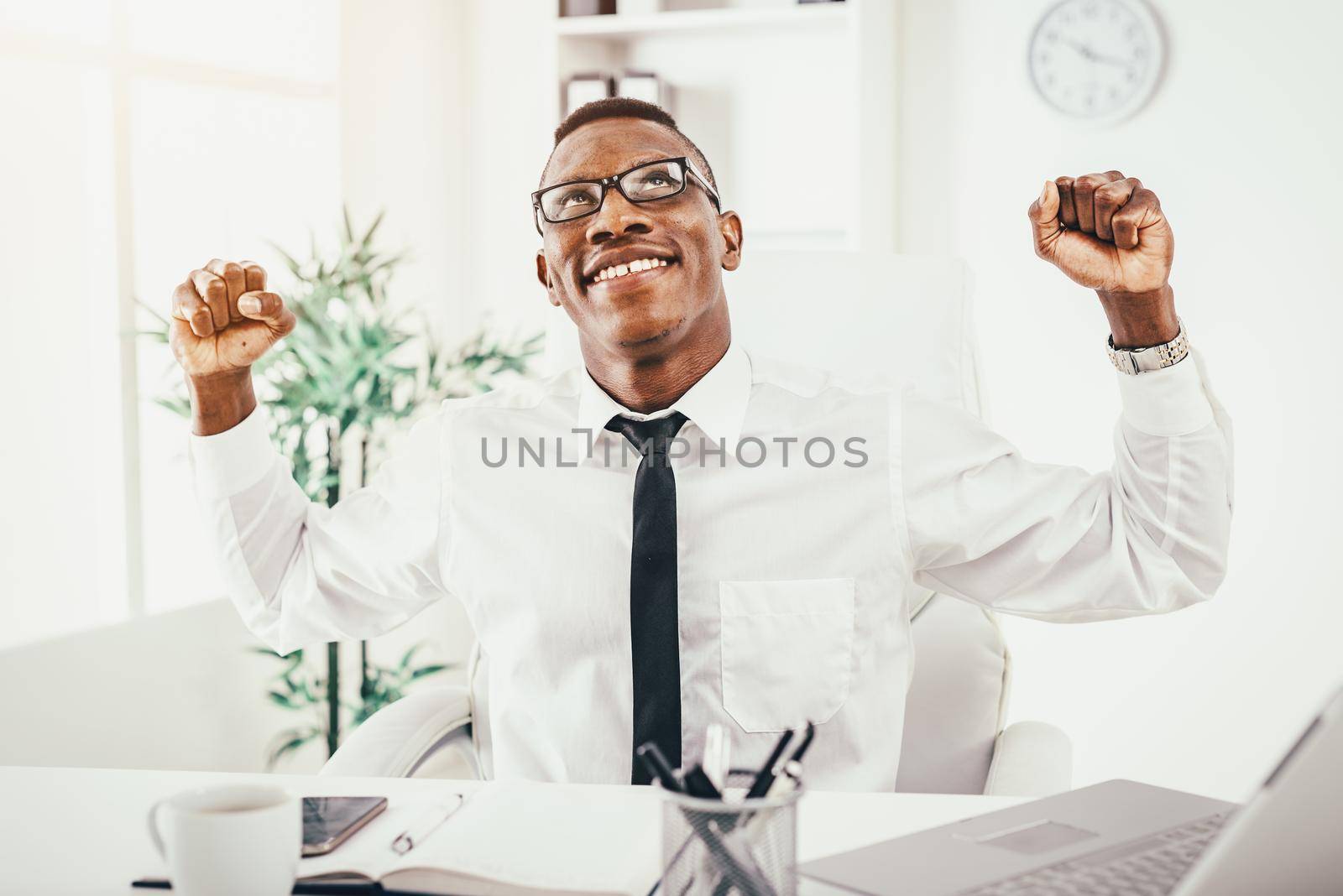 Successful African businessman celebrating success with fists in the modern office.