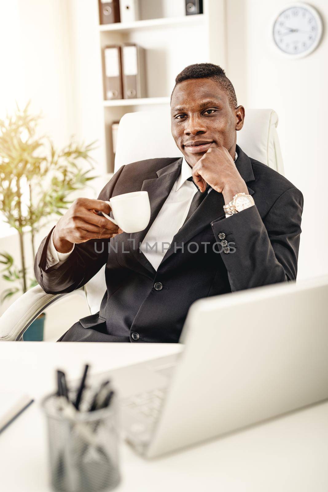 Happy African businessman sitting in the office and drinking coffee.