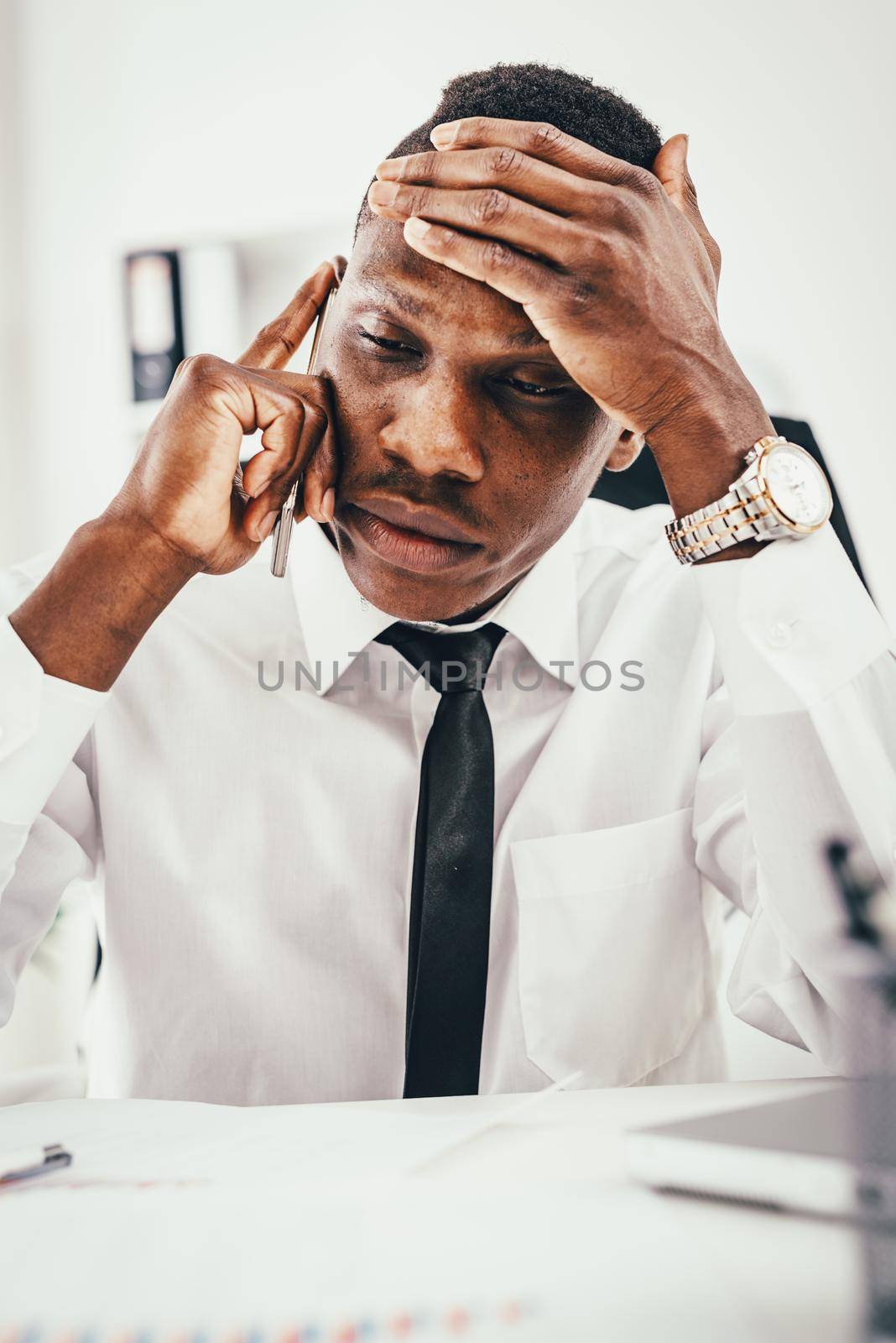 Pensive African businessman talking on smartphone in modern office. 