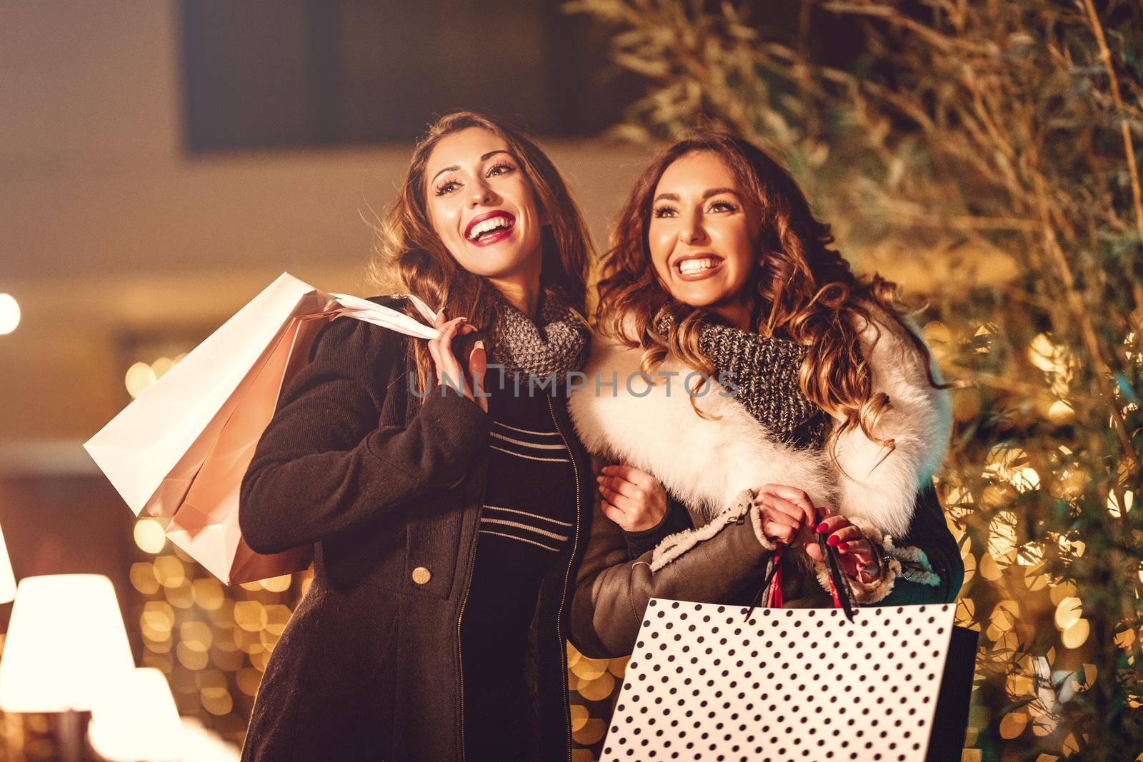 Two female friends enjoy the night in shopping and laughing with shopping bags in their hands.