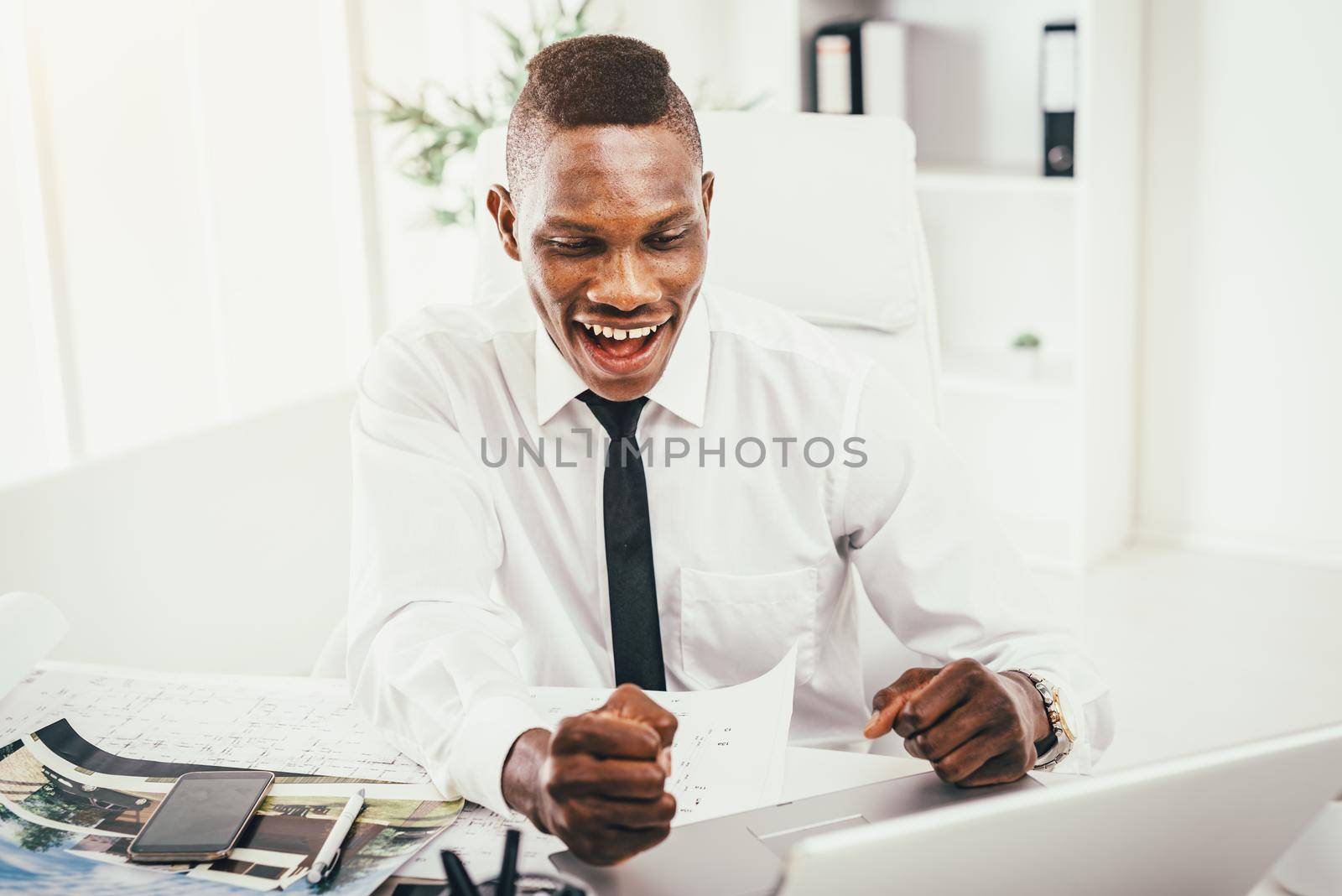 Successful African businessman celebrating success with fists in the modern office.