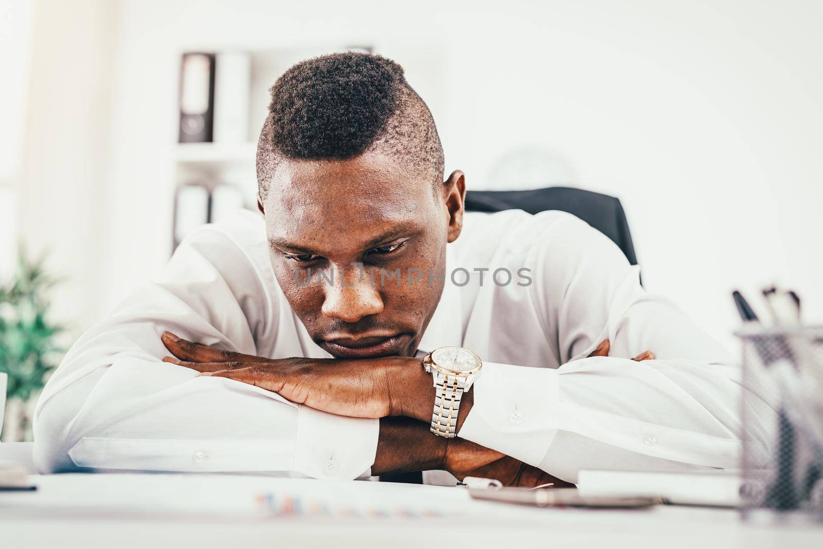 Anxious African businessman sitting in the office and holding his head leaning on his hands on the table