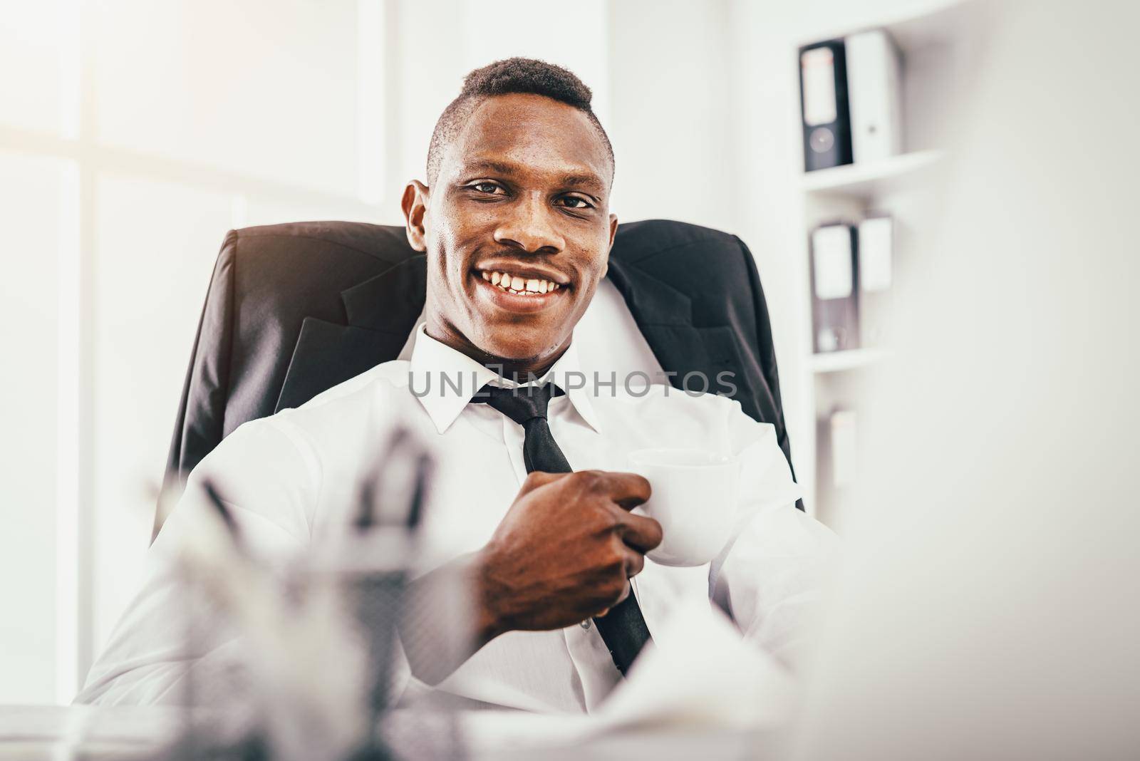 African smiling businessman is sitting in the office satisfied with his work.