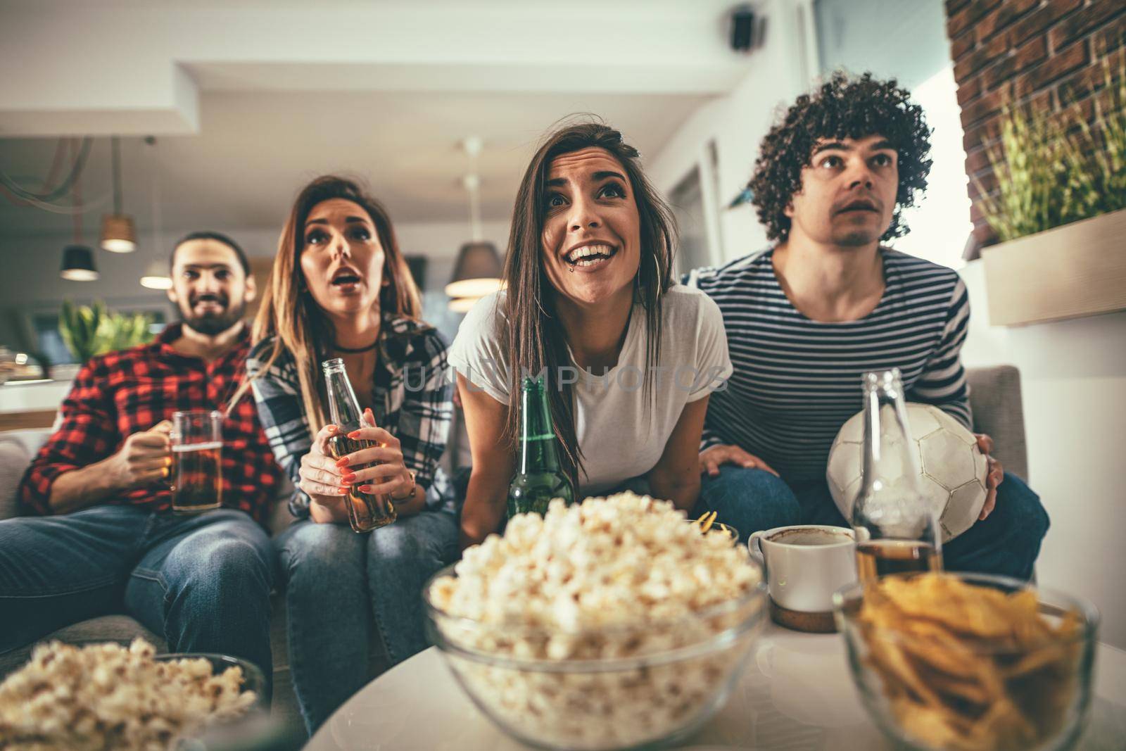 Friends are fans of sports games as football love spending their free time at home together. They are screaming and gesturing for a victory. 