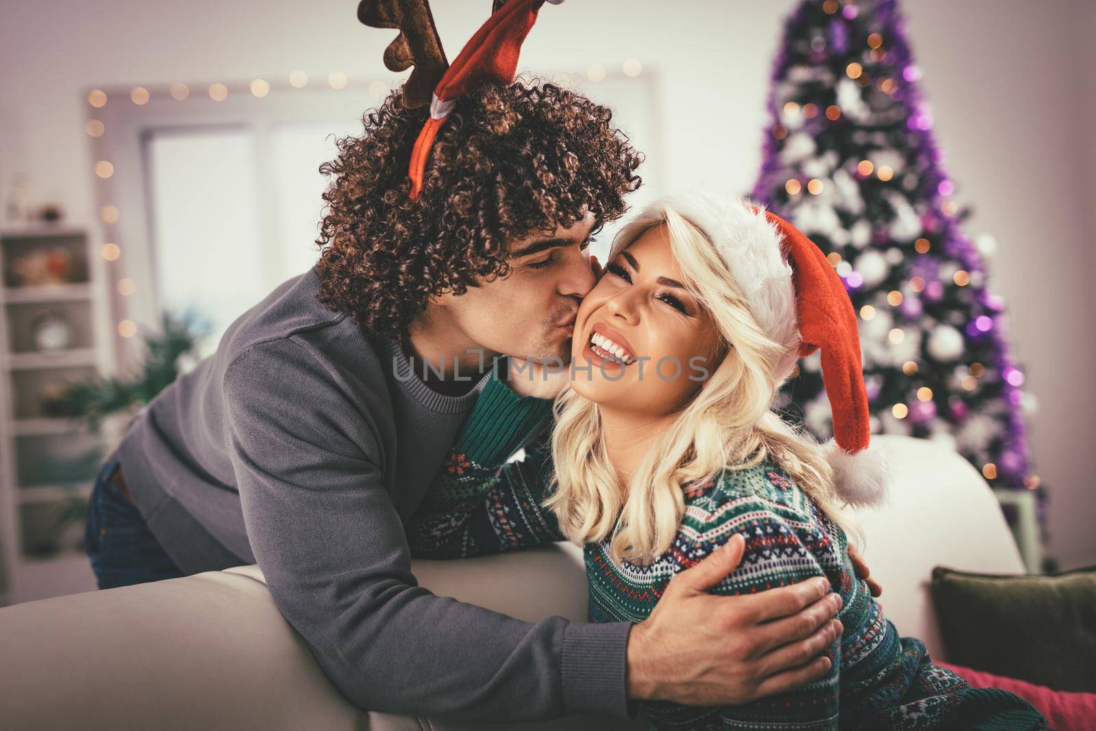 Loving couple in cozy warm sweaters on a Christmas - New Year eve, smiling, kissing, having fun with each other. 