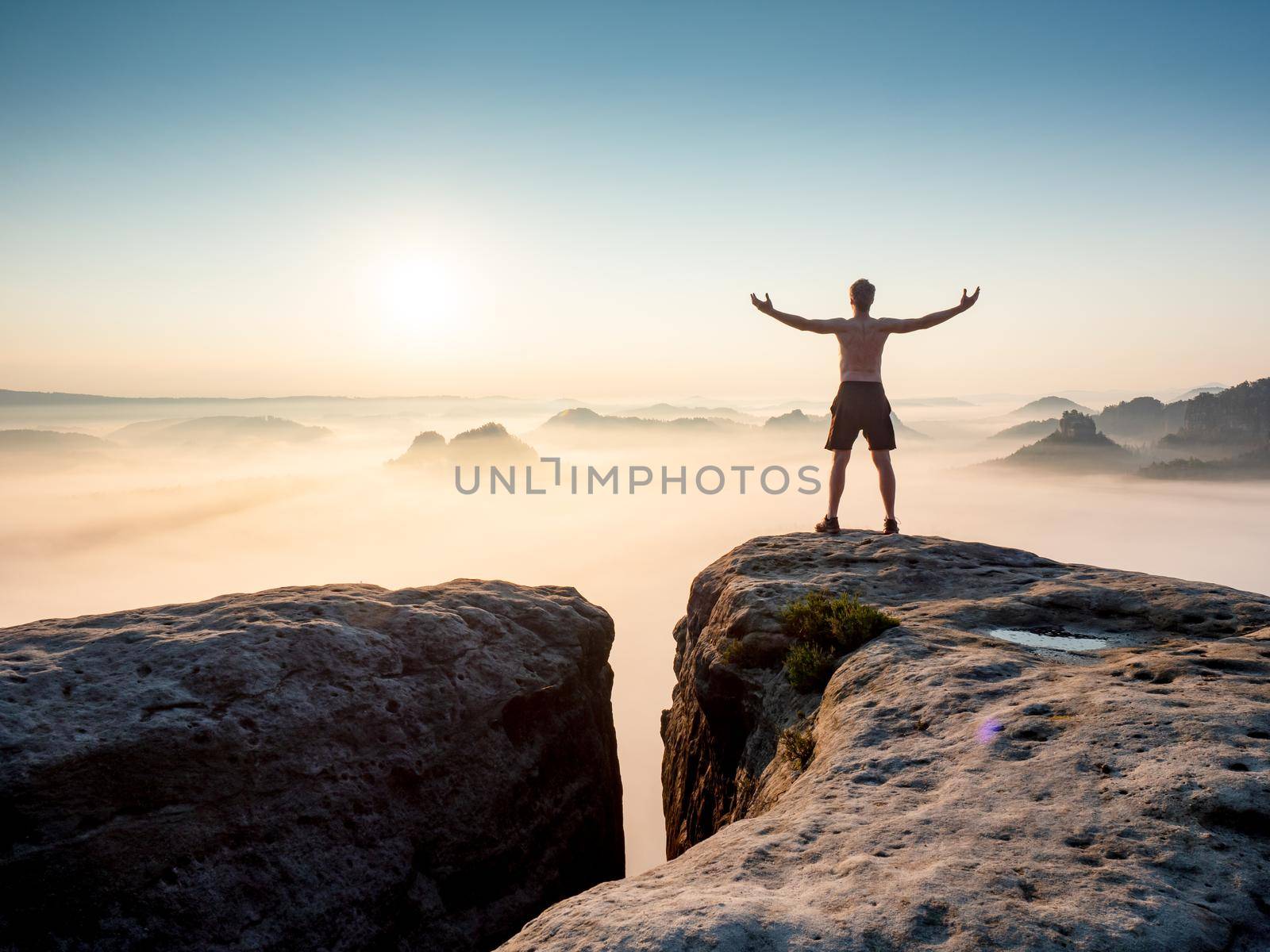 Happy trail runner at rocky view edge raised arms to sun greeting. Nature lover and landscape hiker.