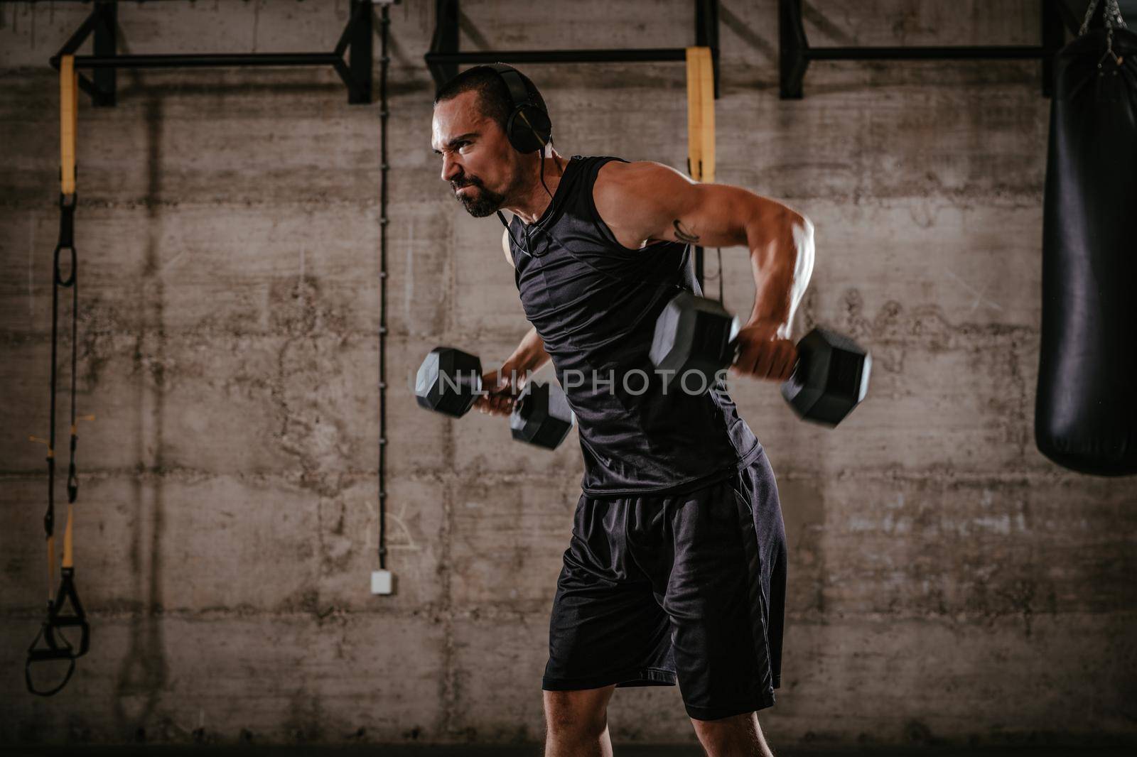 Young muscular man doing hard exercise with dumbbells for shoulders on cross fit training at the gym.