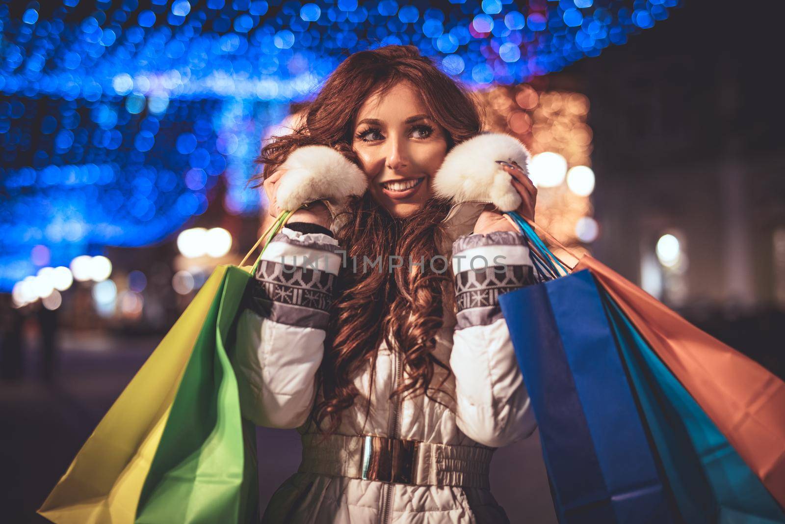 Cheerful young woman with colorful shopping bags having fun in the city street at Christmas time.