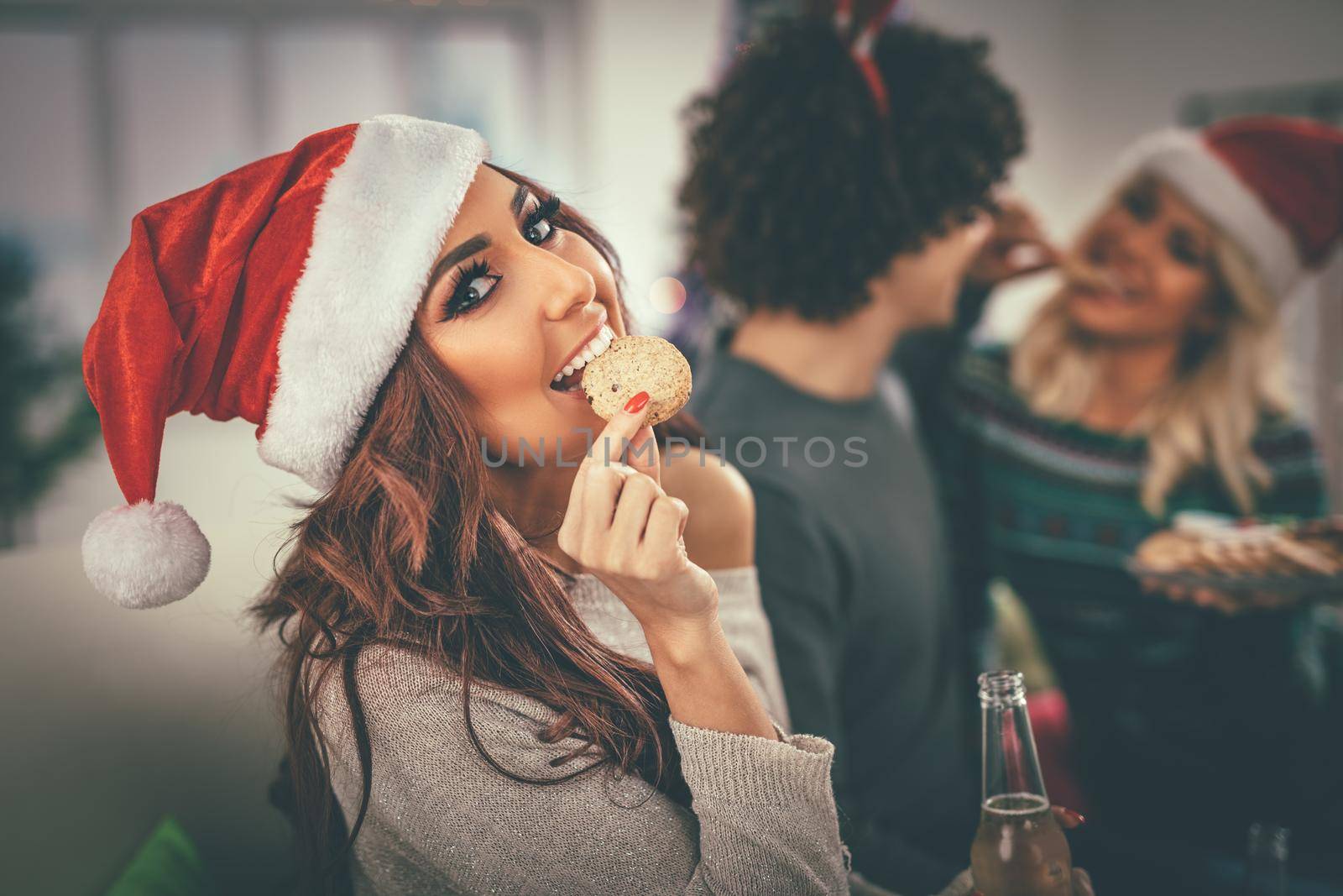 Beautiful smiling woman on Christmas eve eating gingerbread cookie and hold a bottle of beer. Looking at camera.