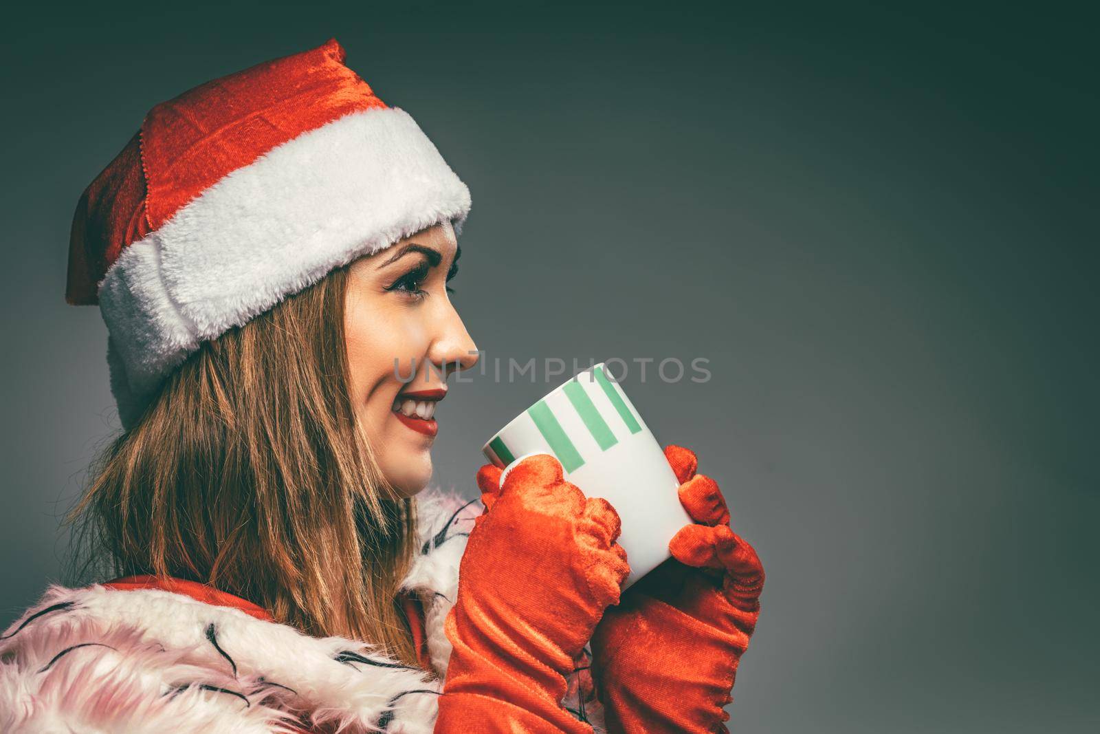 Portrait of a beautiful young smiling woman in Santa Claus costume. She is smiling and holding cup of hot tea.