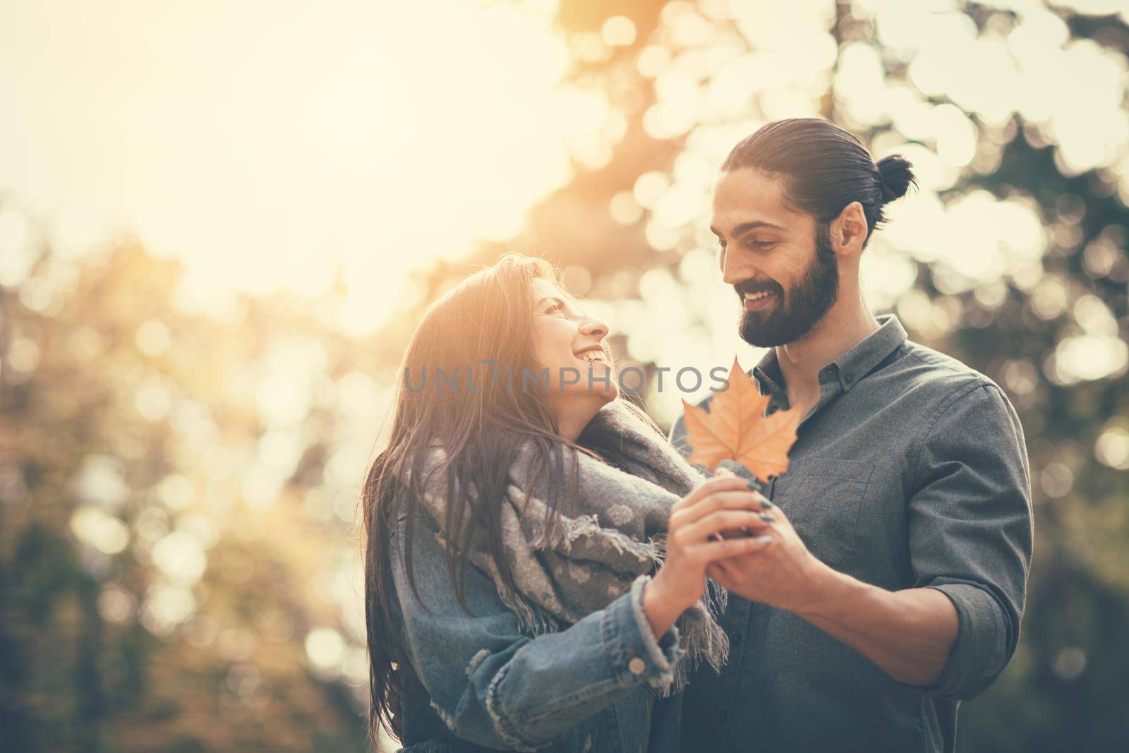 Portrait of a beautiful young couple in sunny forest in autumn colors. They are embracing and holding yellow leaf.
