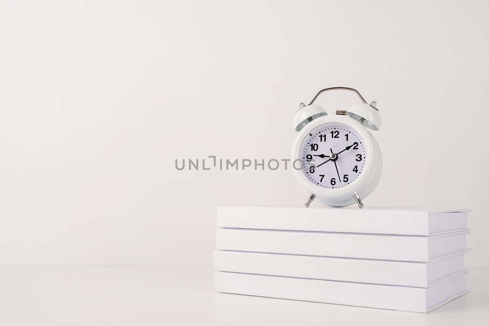 Time management, punctuality, business metaphors. Back to school. White alarm clock hands on nine ten on stack of books, mockup design, copy space