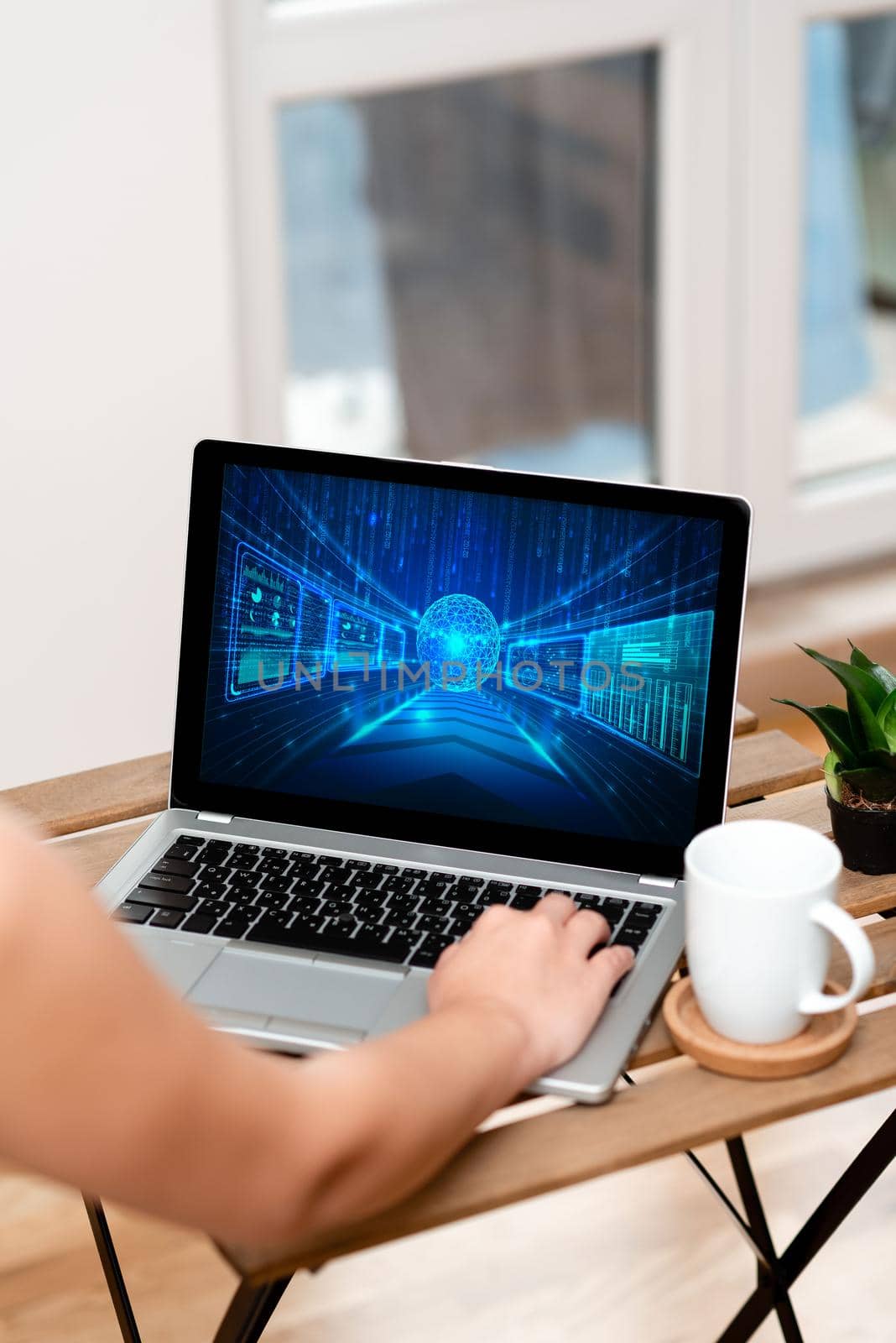 Hand Busy Typing On Laptop Beside Coffe Mug And Plant Working From Home.