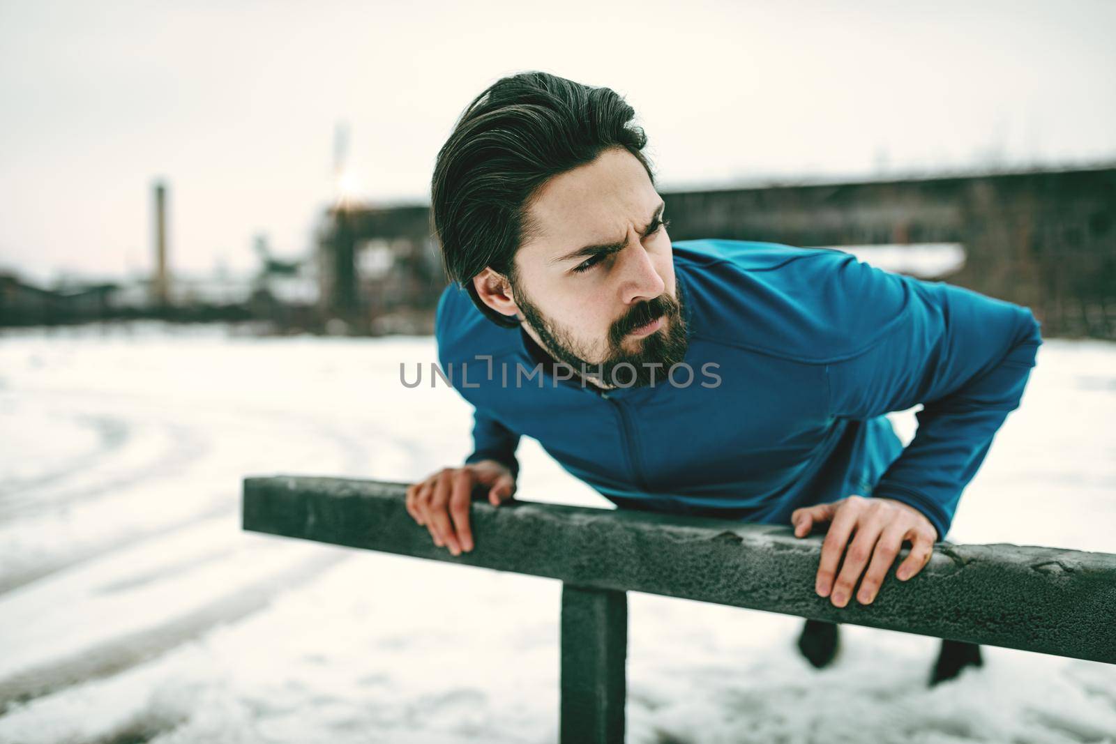 Young man athlete doing push ups and doing exercises during the winter training outside in while it snowing. Copy space.