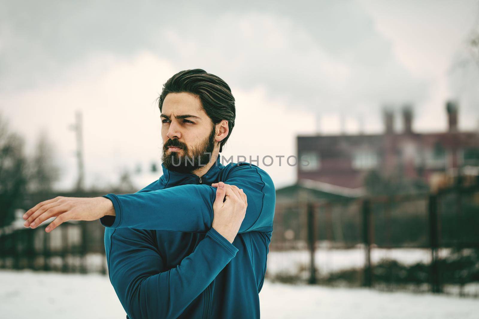 Active young man stretching and doing exercises in the old factory place among old railroad during the winter training outside in. Copy space. 