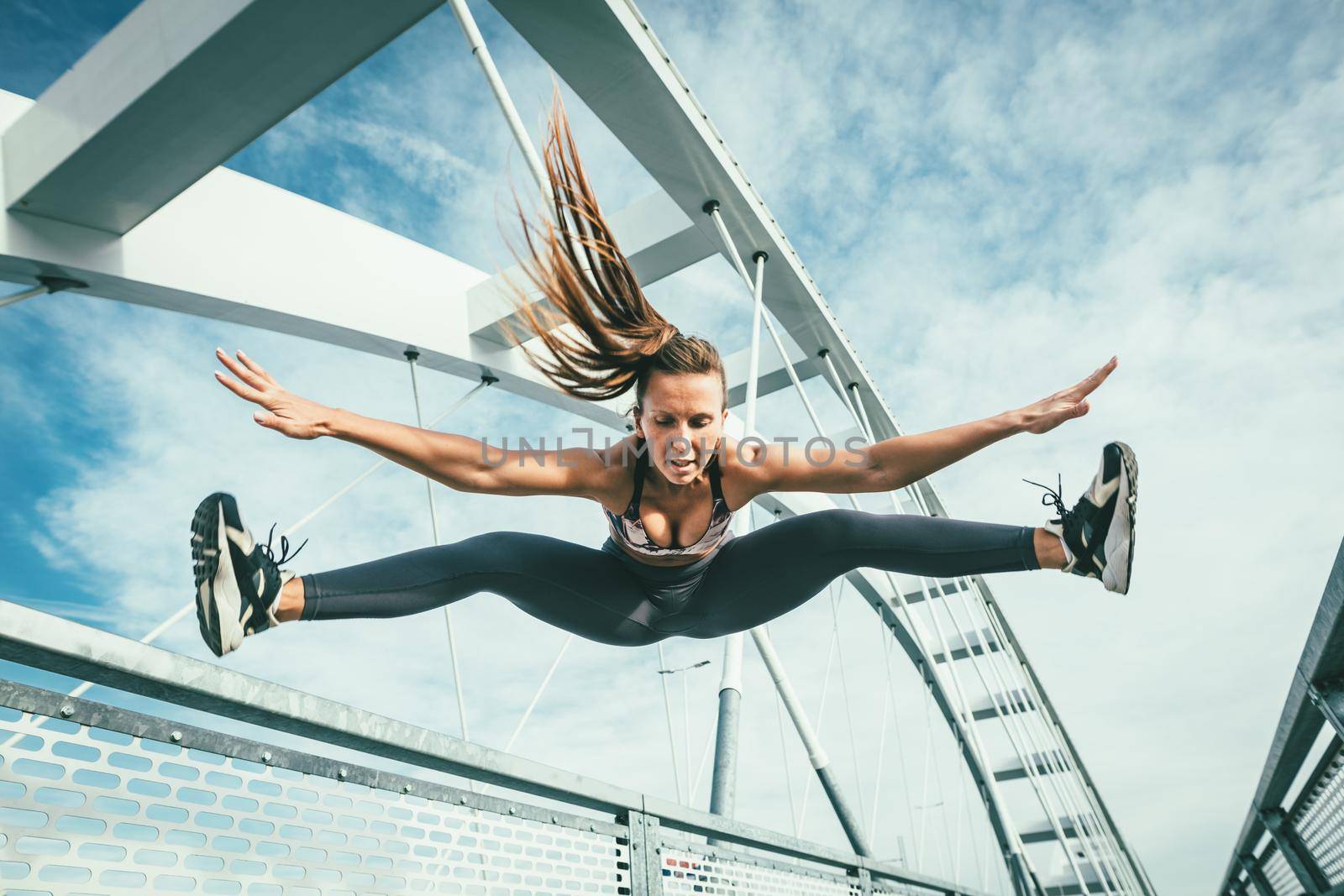 Beautiful young woman jumping after successful training on the river bridge.