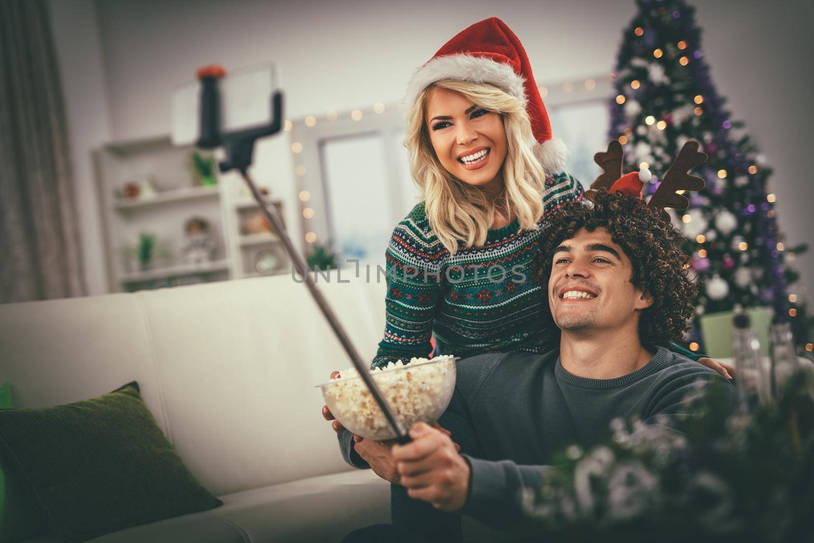Loving couple in cozy warm sweaters on a Christmas - New Year eve, smiling and having fun taking selfie and eating popcorn.  