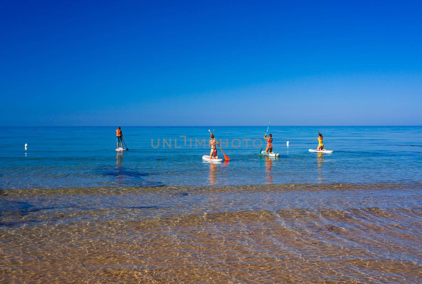 Stand up paddle boarding. Joyful group of friendsare training SUP board in the mediterranean sea on a sunny morning in Realmonte beach by bepsimage