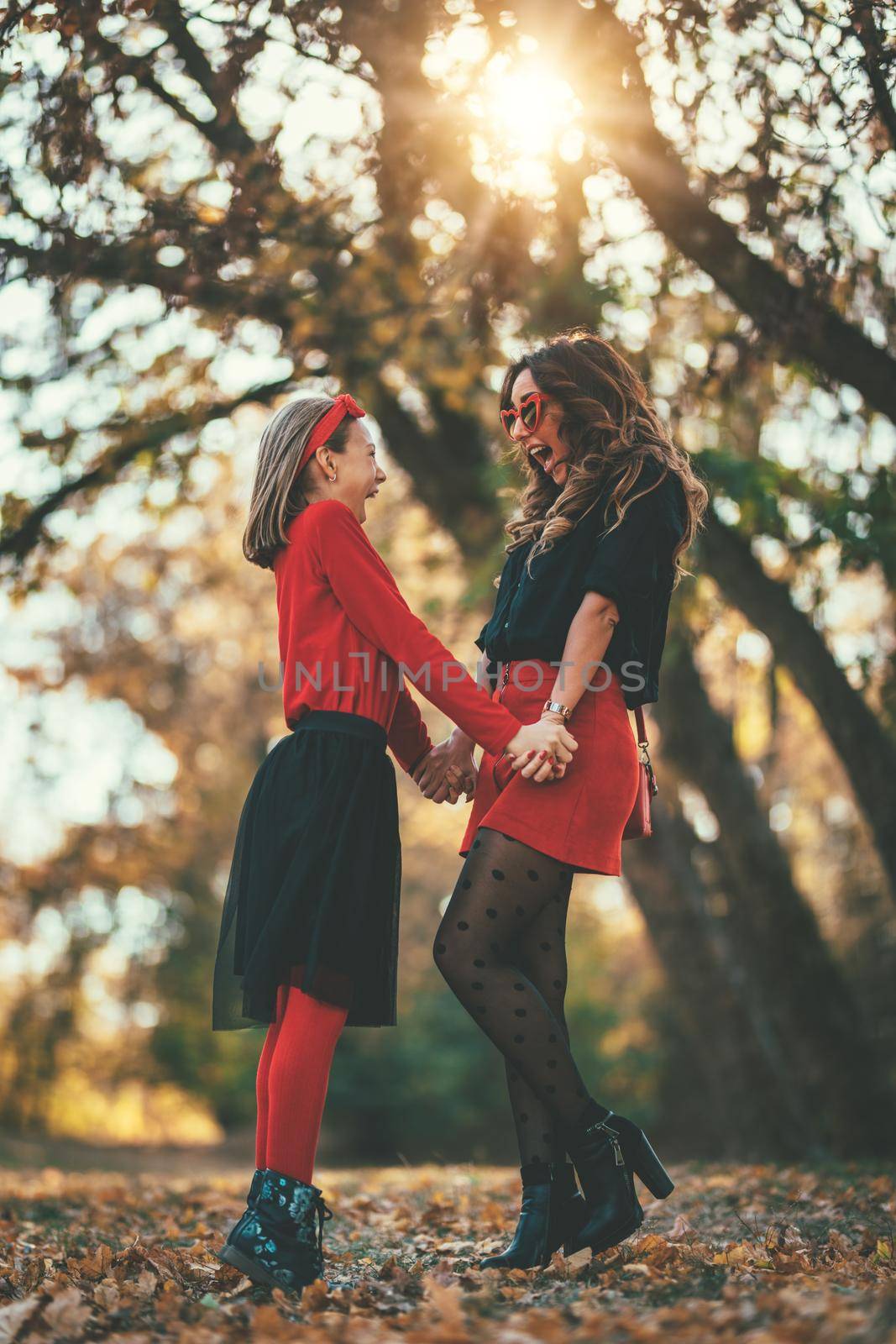 Beautiful young mother and her happy daughter having fun in the forest in sunset. They are holding hands, laughing and looking each other.