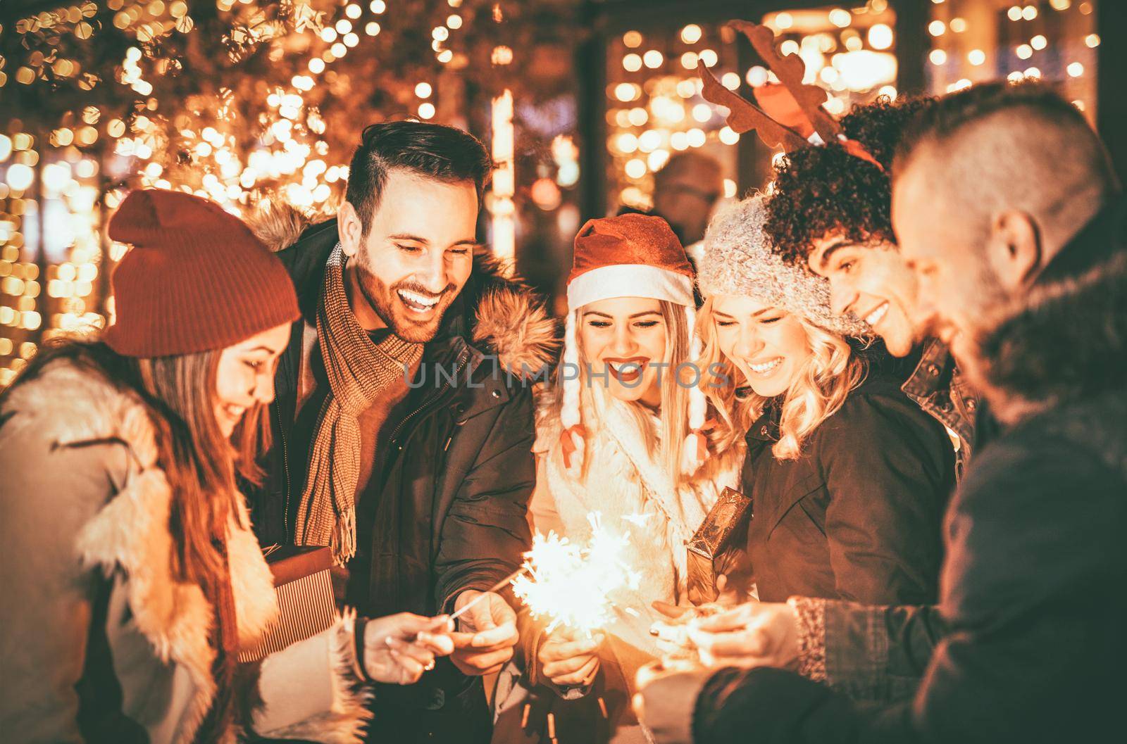 Group of happy young friends having fun with sparklers on night Christmas party.