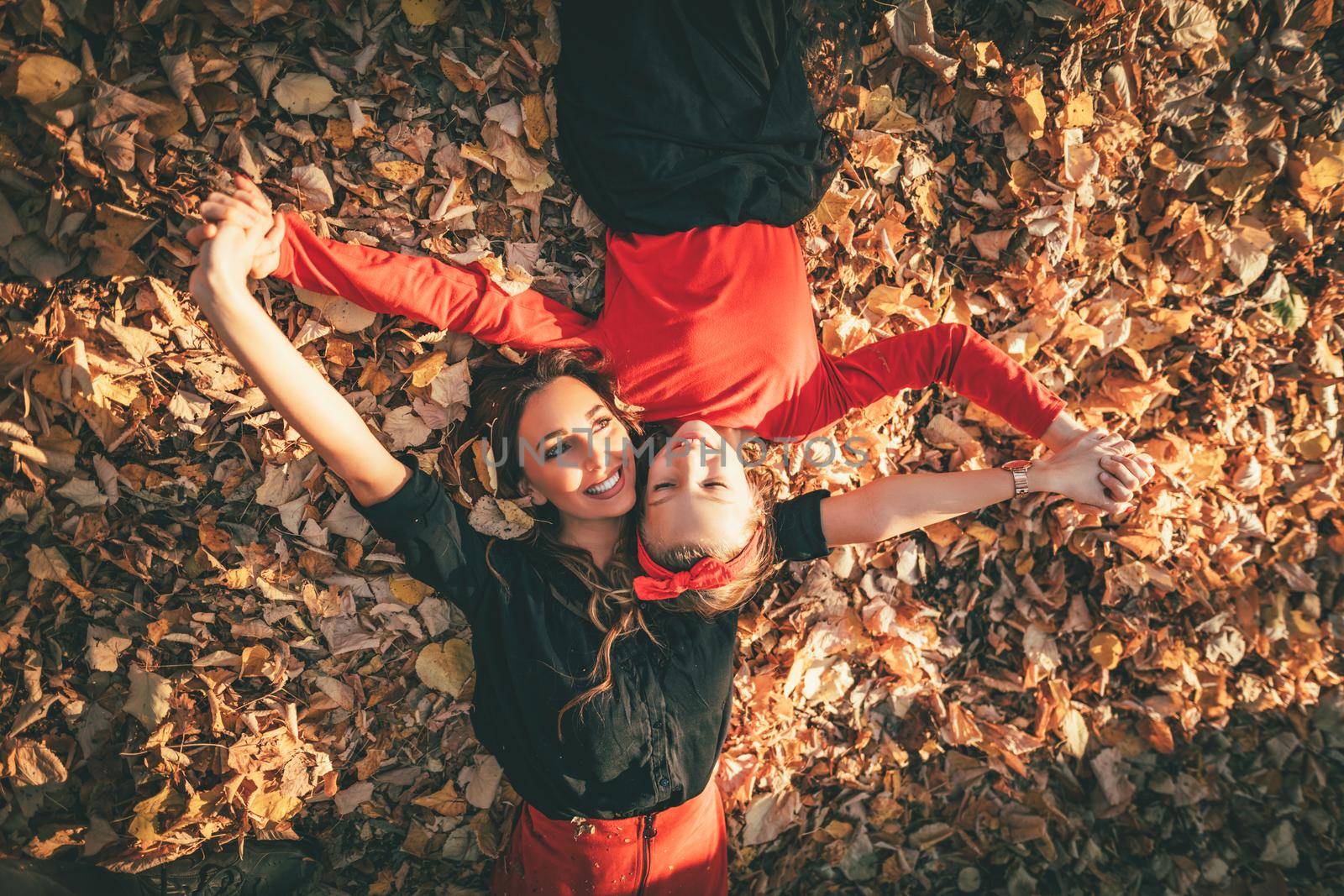Beautiful young woman and her little daughter are enjoying in autumn sunny forest colors. They are lying down on golden yellow leaves and having fun. 