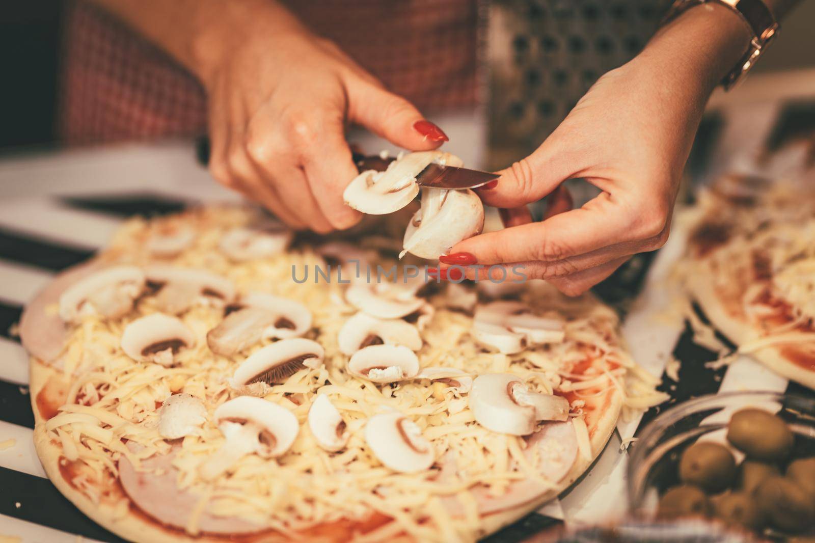 Close-up of a young women's hands cutting mushrooms and putting on the pizza dough.