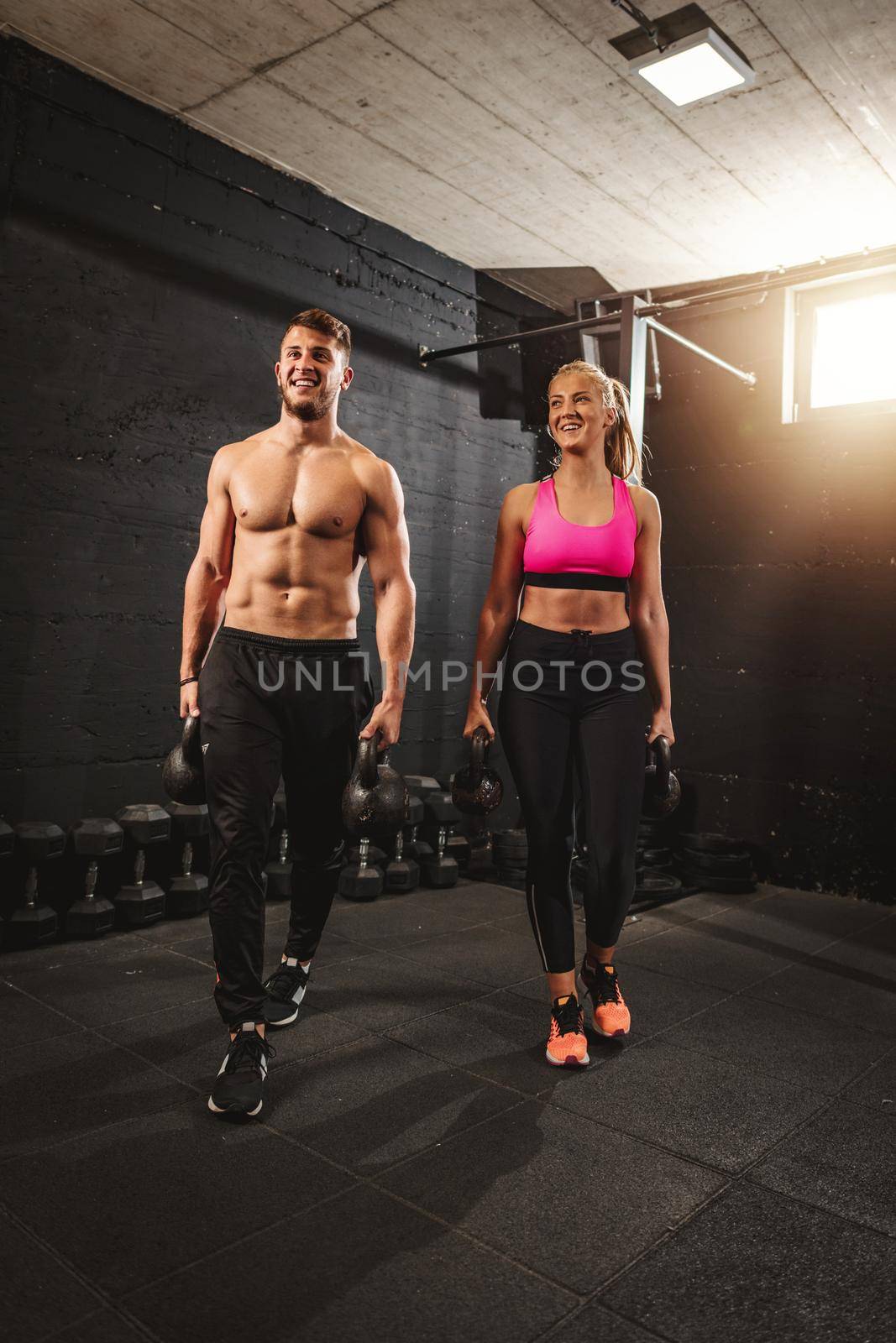 Young muscular couple are ready to do hard exercise with kettlebells on cross training at the gym.