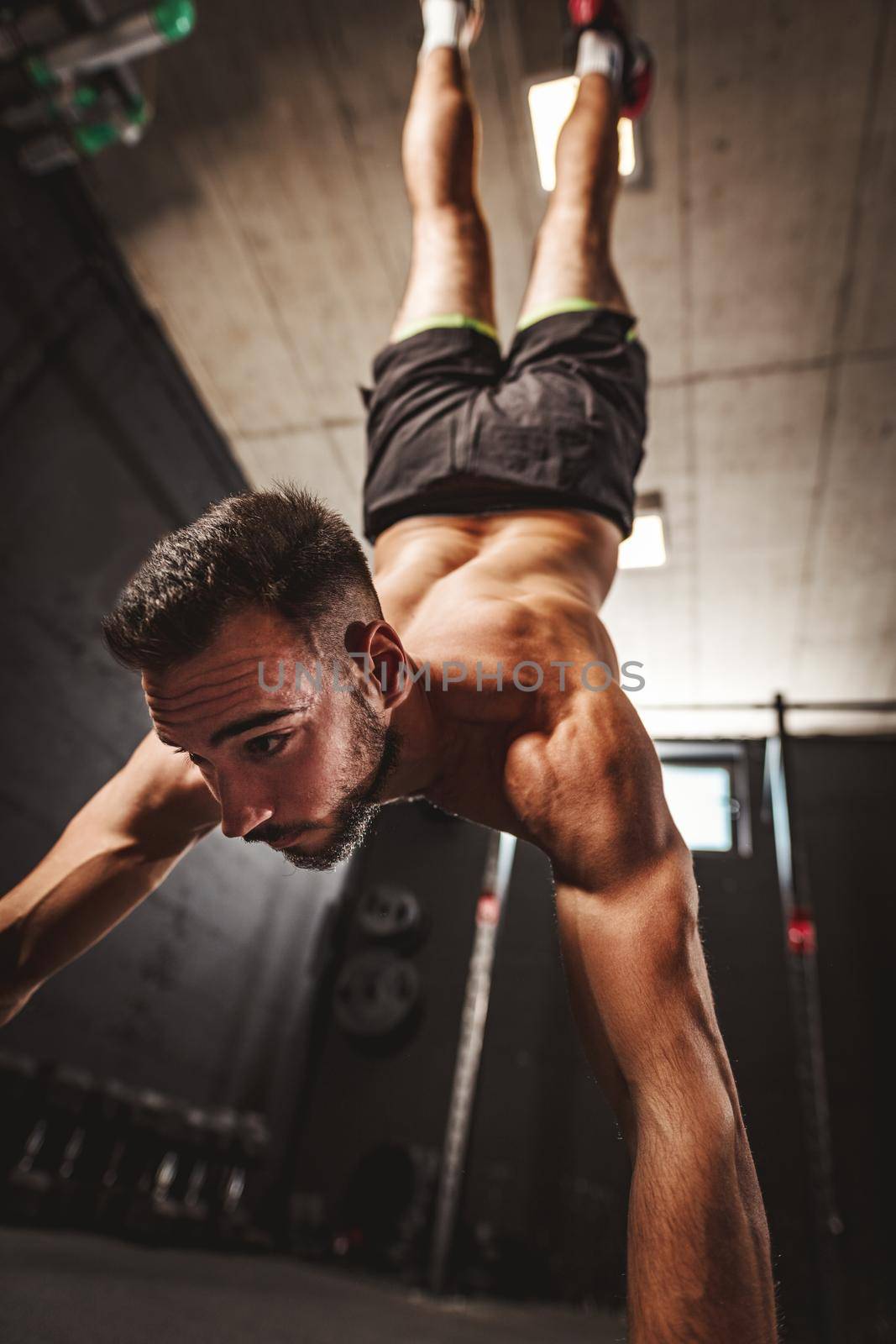 Young muscular man doing hard exercise at the gym. His is doing handstand and whole weight is on his hands.