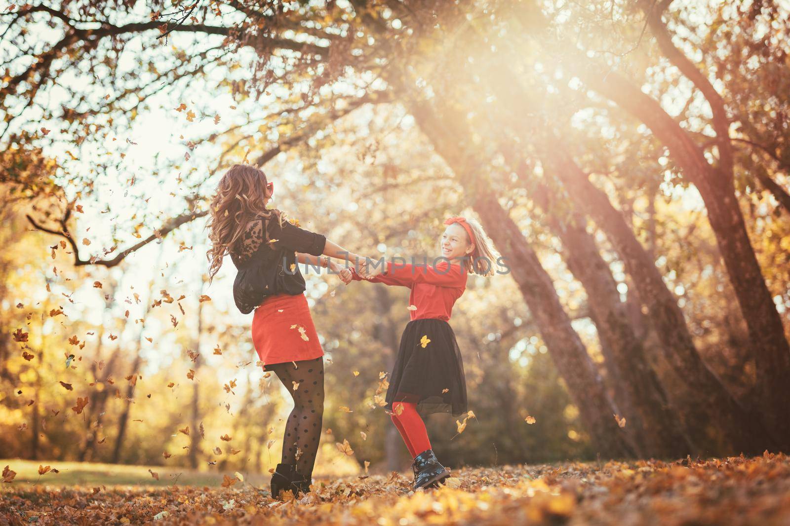 Beautiful young mother and her happy daughter having fun in the forest in sunset. They are holding hands, laughing and turn around.