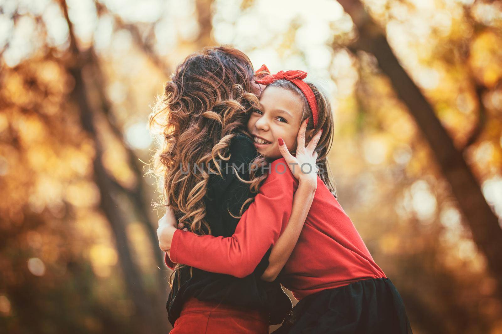 Beautiful young mother and her happy daughter having fun in the forest in sunset. They are hugging each other and smiling.