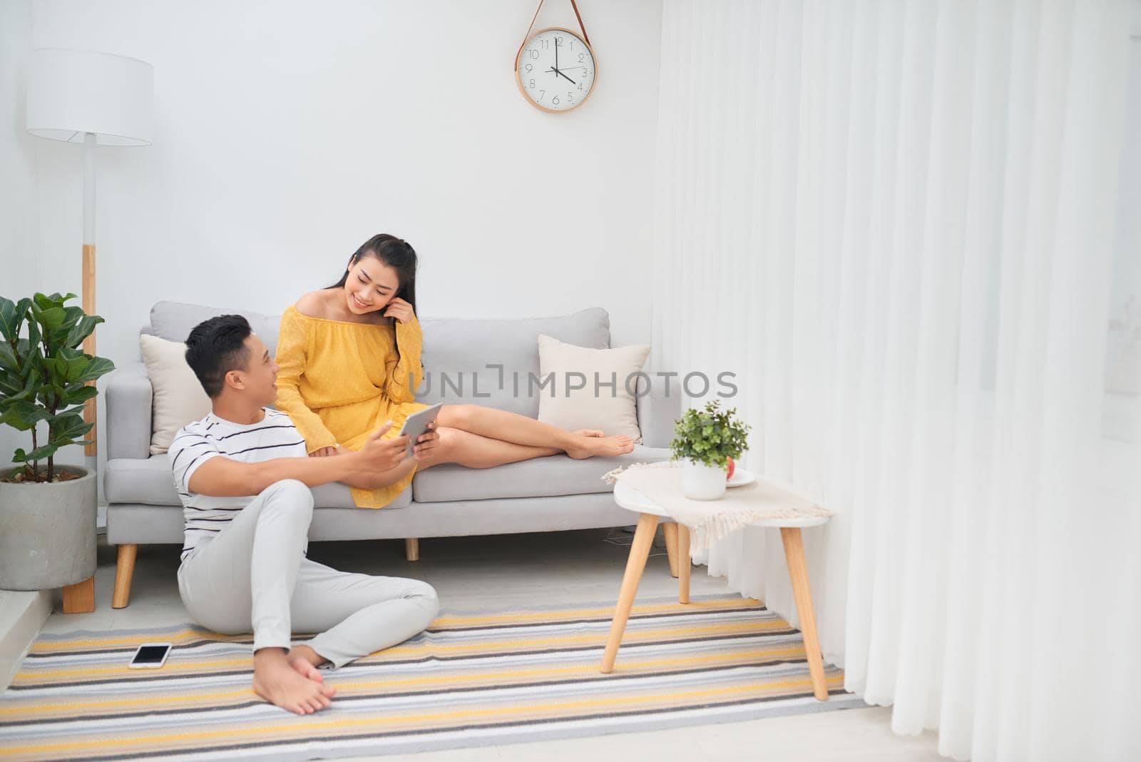 Young asian couple sitting on couch at home, using a tablet PC for Internet and social media. 