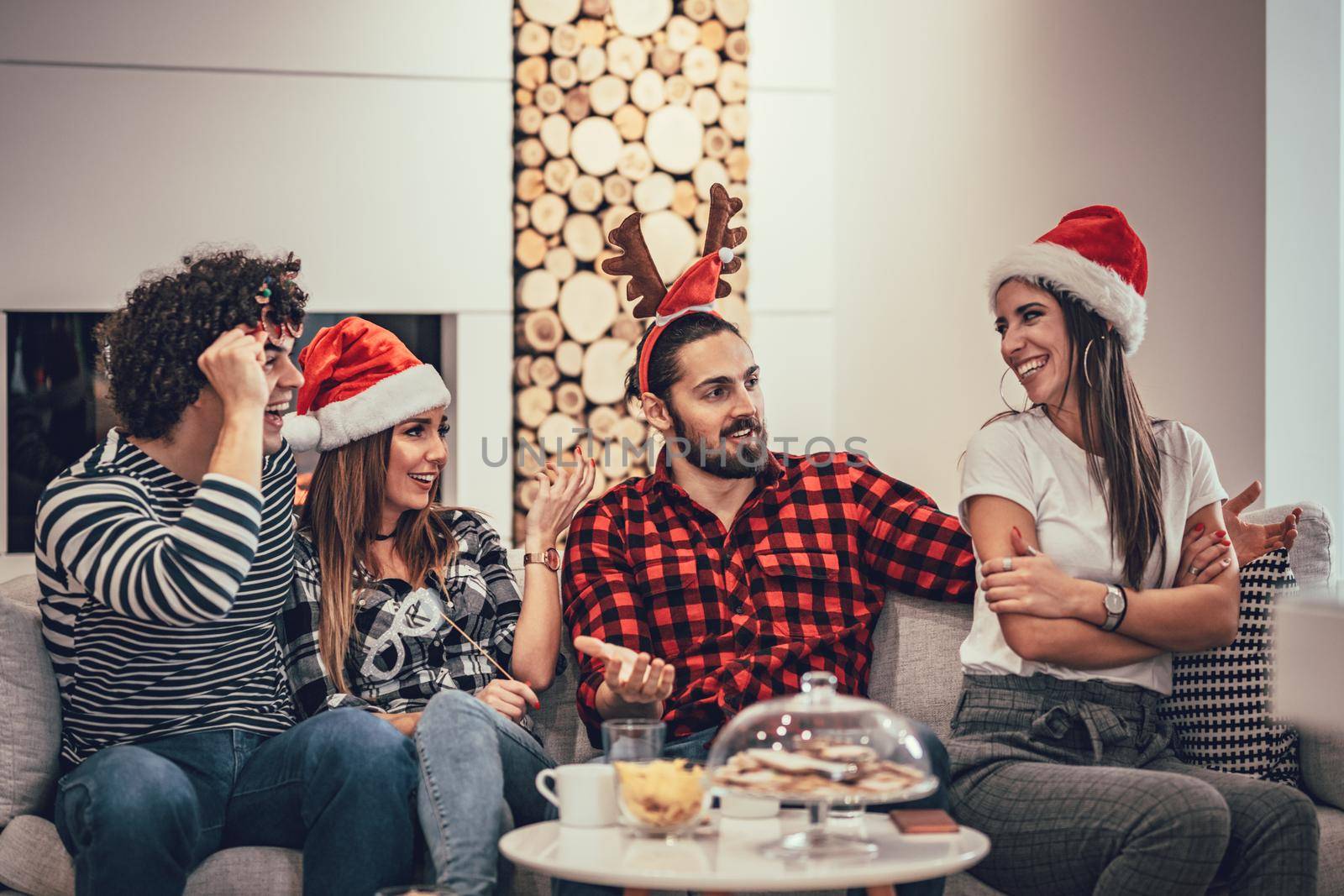 Happy beautiful friends spending New Year eve at home sitting on sofa and talking. They have great holidays having fun in nice company indoors. 