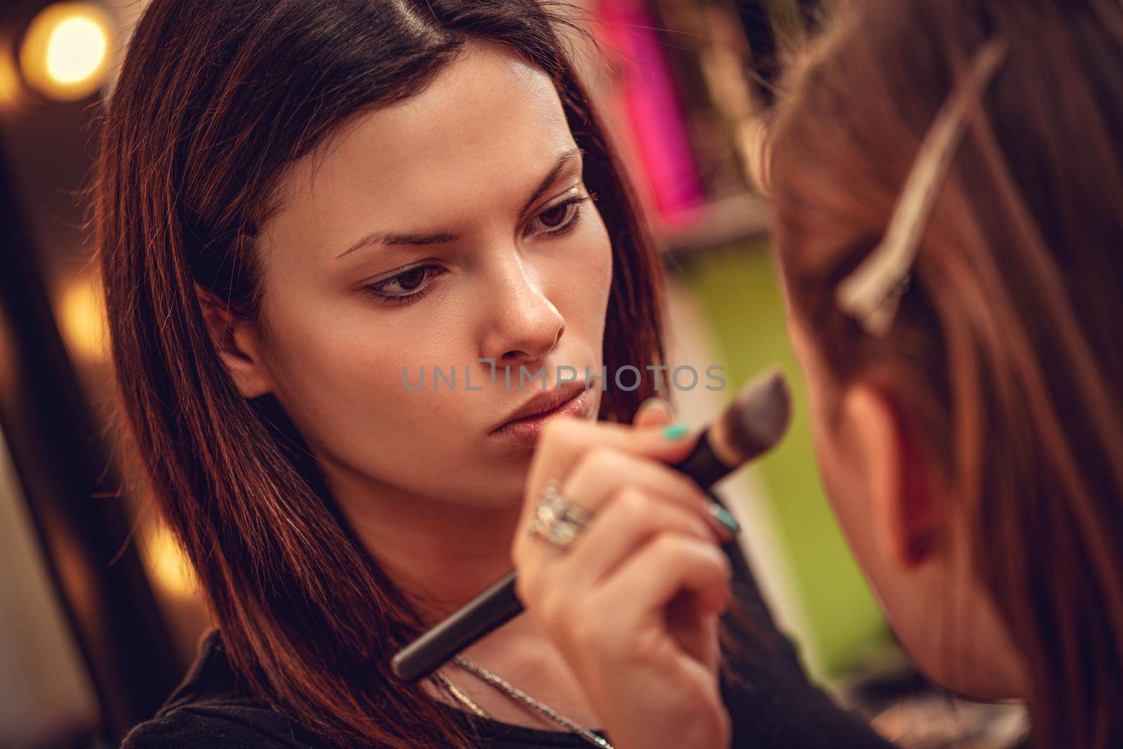 Makeup artist contouring beautiful girl's face with makeup brush. Close-up. 