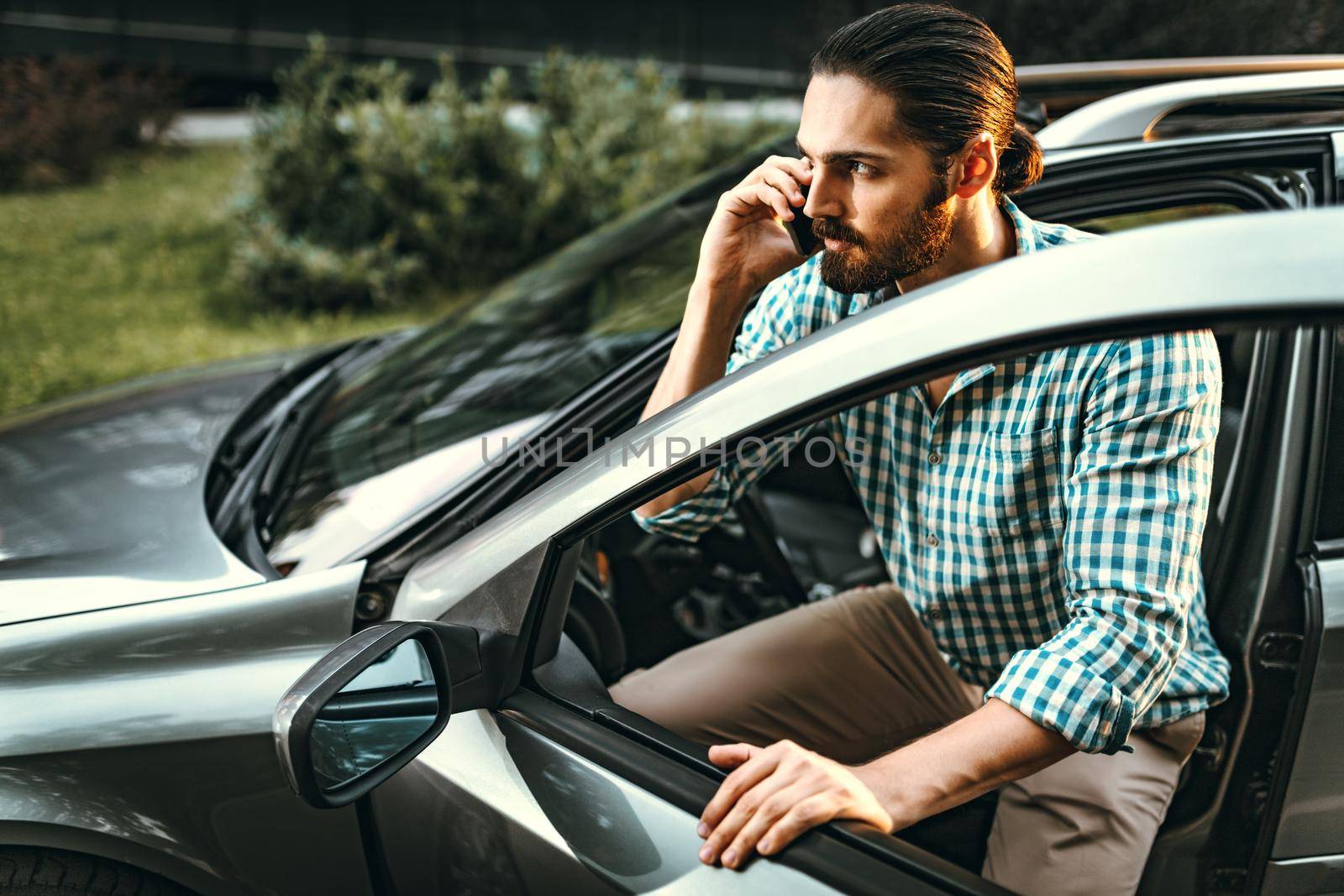 Young confident businessman holding smartphone in his hand and is talking, during is going to sit in the car.