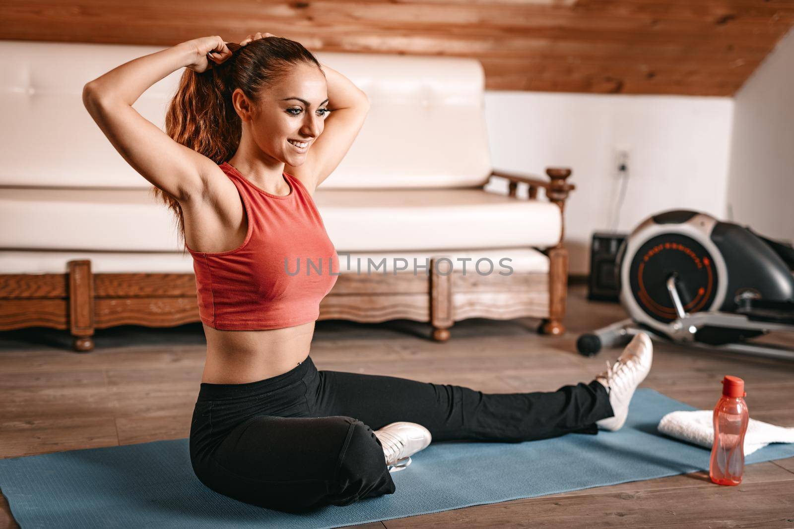 Beautiful young woman getting ready for workout at home. She is binds the hair in a ponytail and doing stretching exercises.