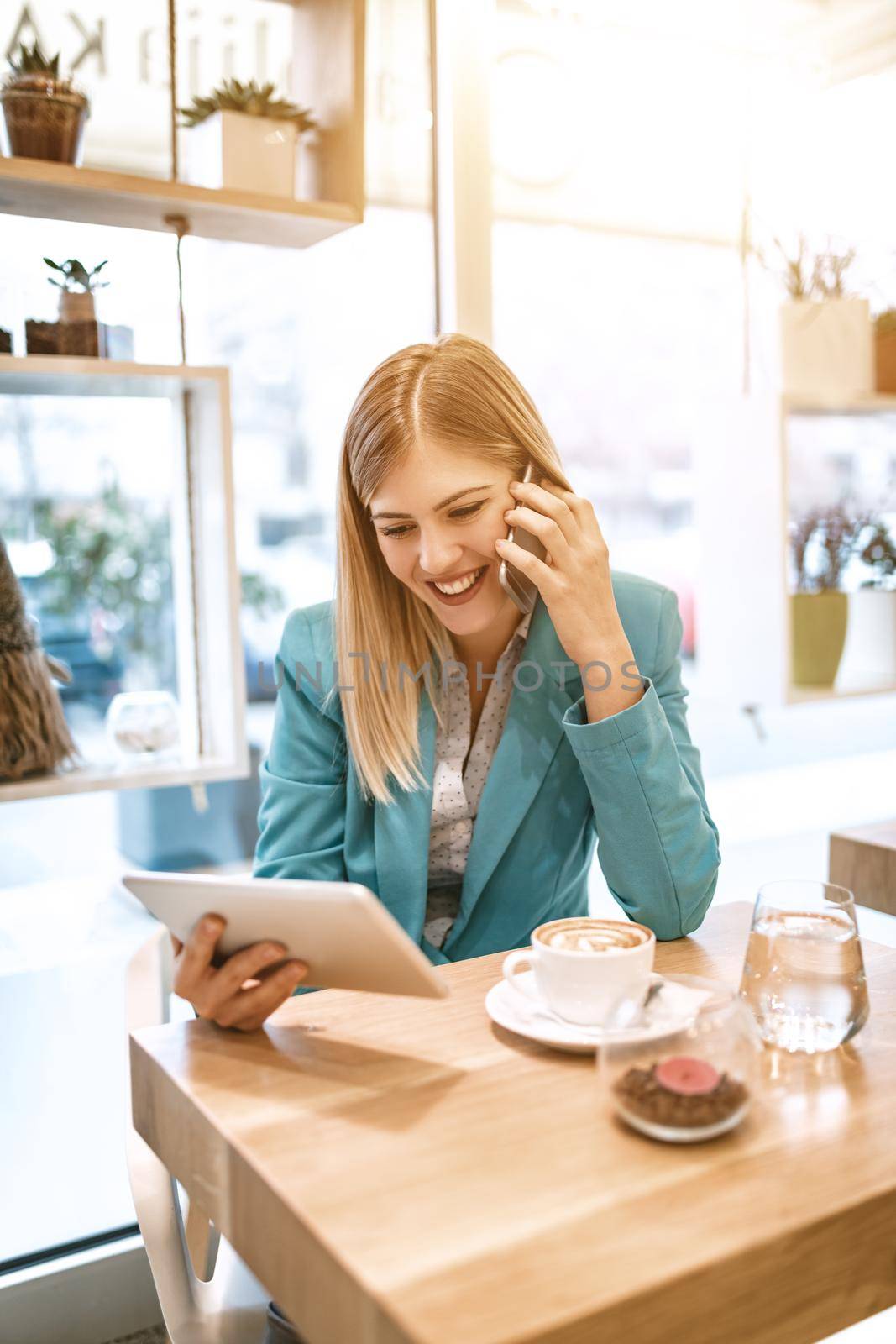 Young smiling businesswoman on a break in a cafe. He is drinking coffee and using smartphone. 