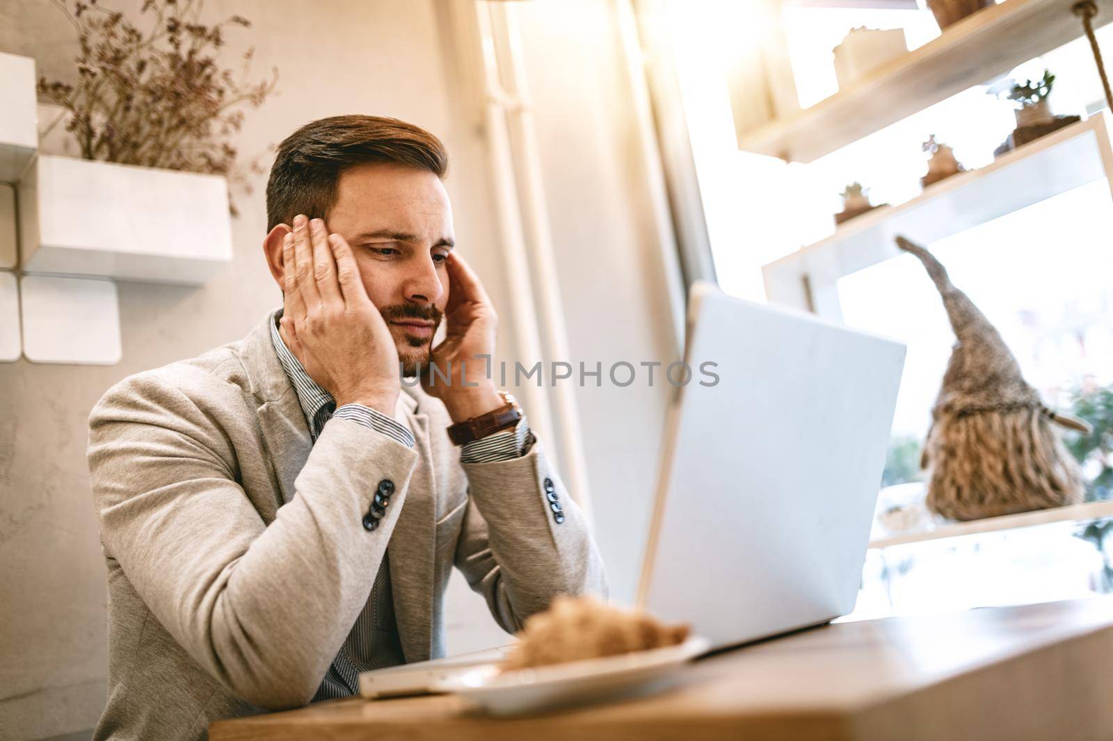 Young stressed businessman on a break in a cafe. He is working at laptop and thinking. 